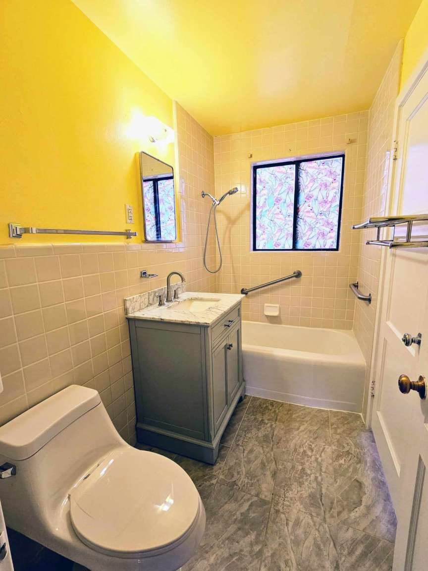 Bathroom with beige tile, a gray vanity, bathtub, and patterned window curtains.