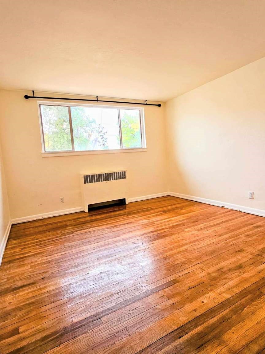Vacant room with polished hardwood floors, a wide window, and a wall heater.