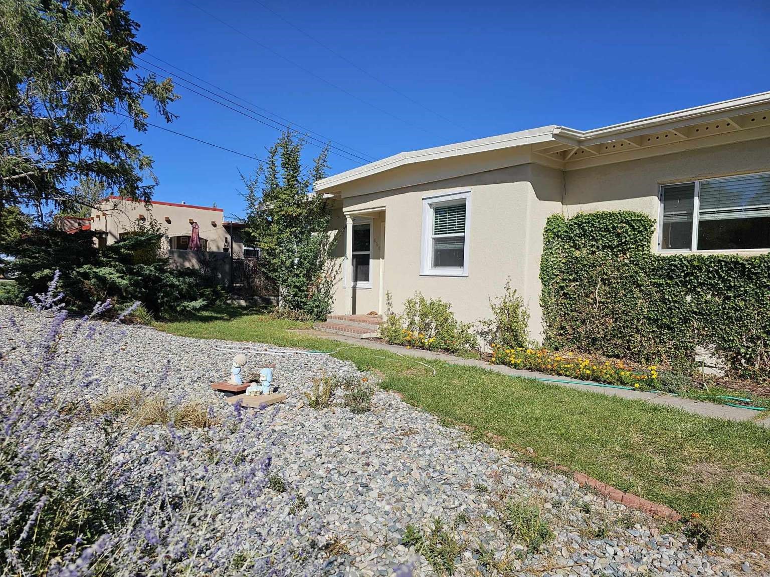 Single-story stucco home beside a rock garden with flowering plants and lawn.