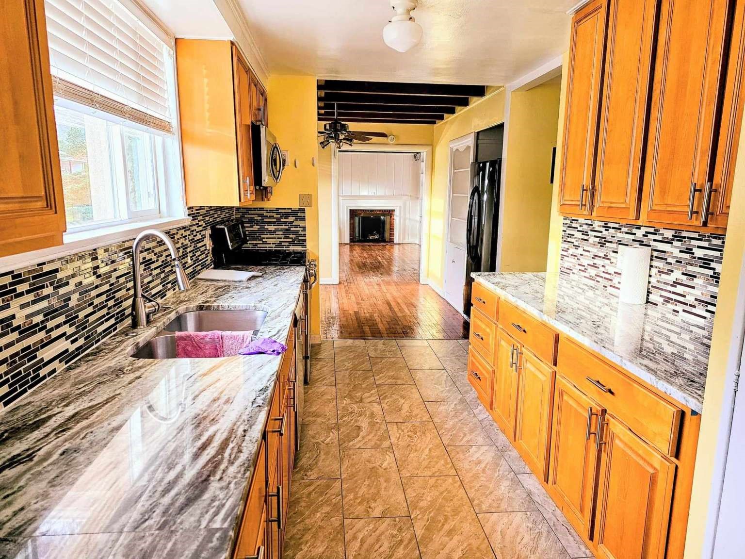 Kitchen with honey-colored cabinets, granite counters, mosaic backsplash, and a view toward a living room fireplace.