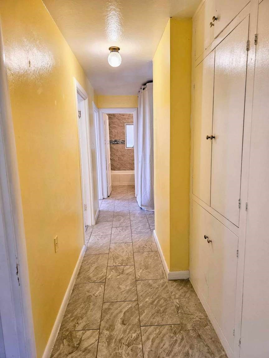 Hallway with yellow walls, tiled flooring, white built-in cabinets, and a bathroom at the far end.