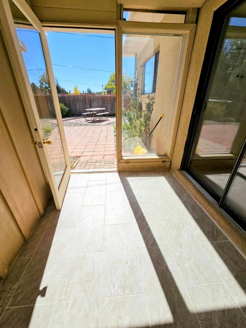Tiled sunroom with glass doors opening onto a sunny patio and picnic table.