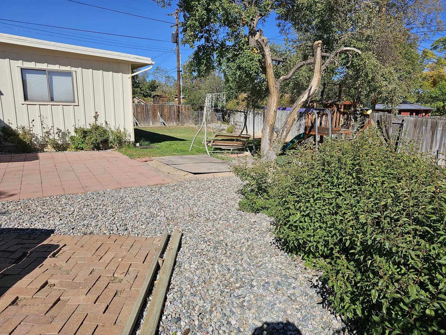Fenced backyard with a gravel path, brick patio, lawn, and garden swings.