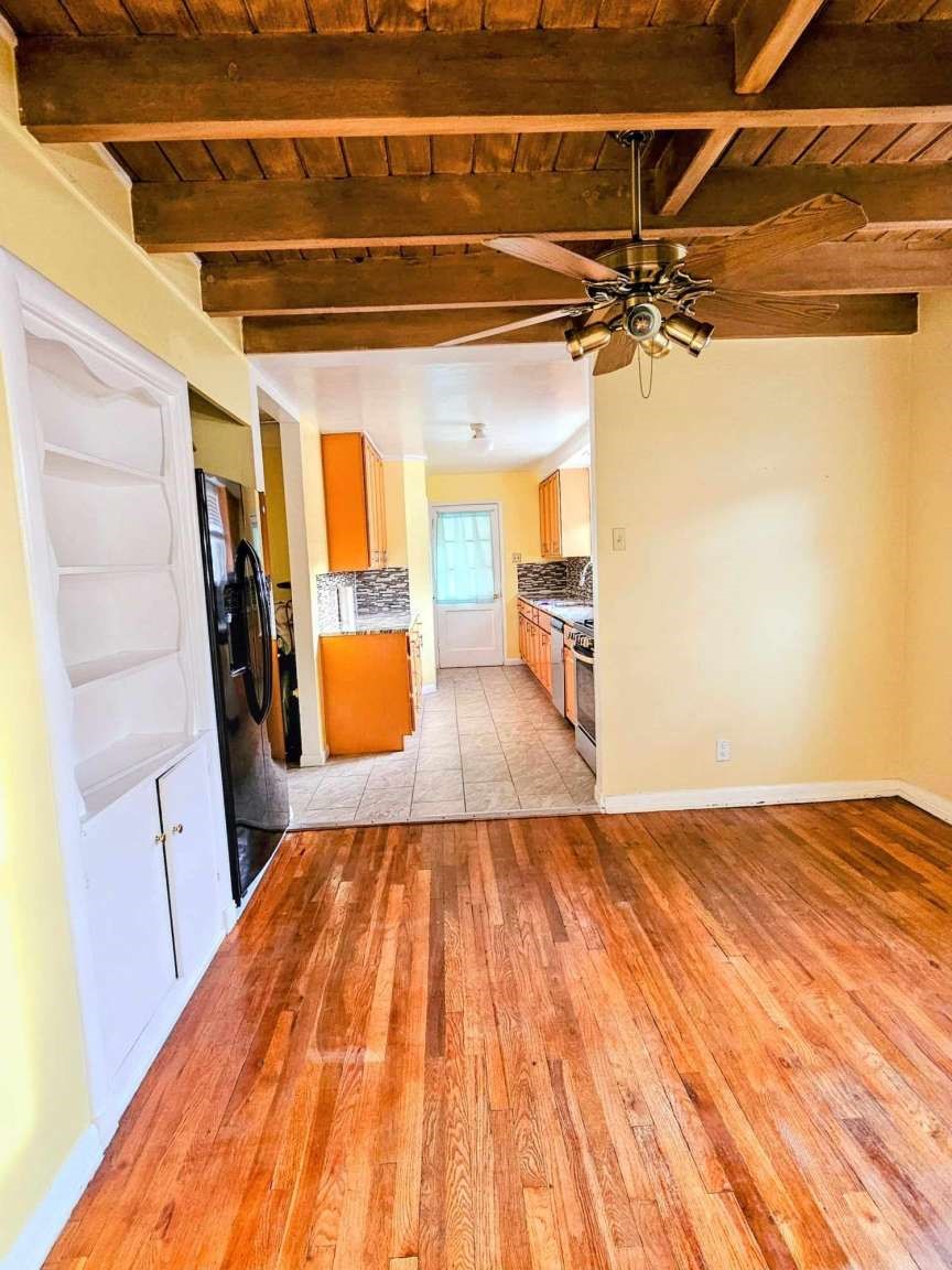 Living area with hardwood floors and exposed ceiling beams, opening into an orange-cabinet kitchen.