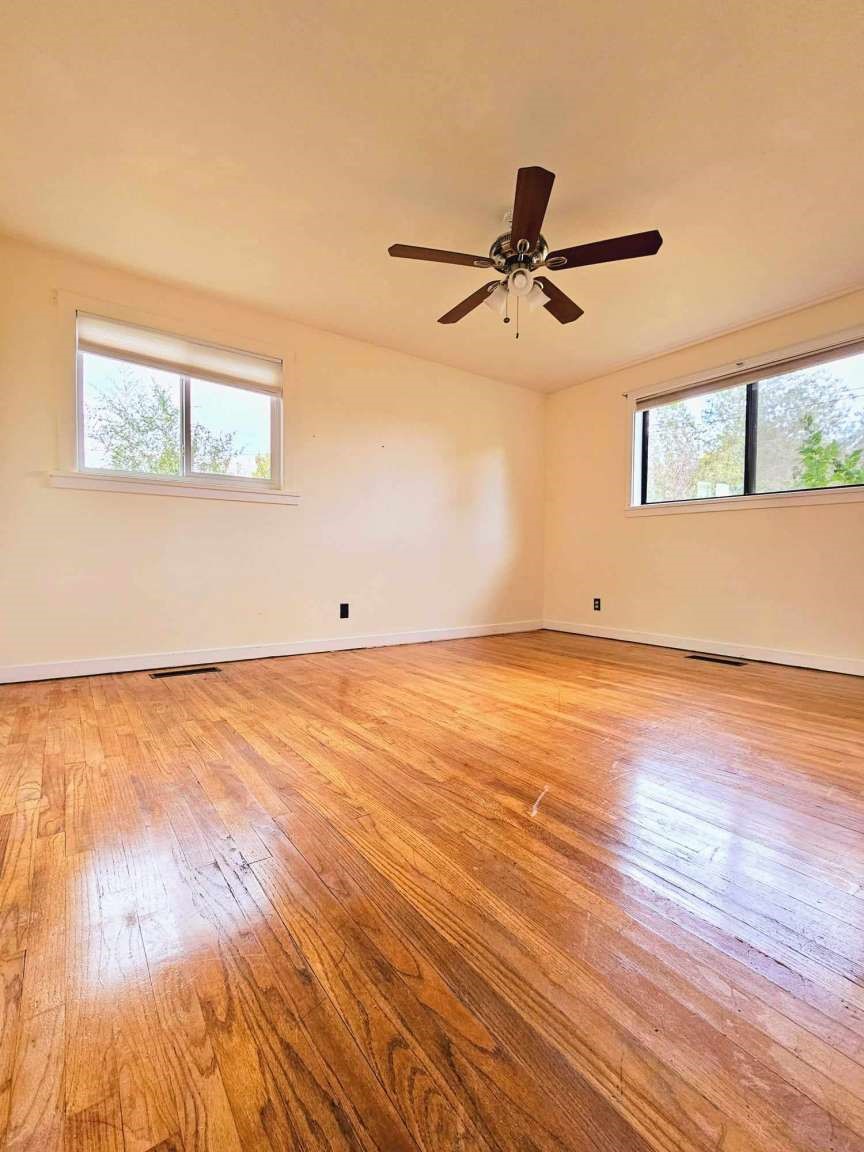 Empty room with polished hardwood floors, two windows, and a ceiling fan.