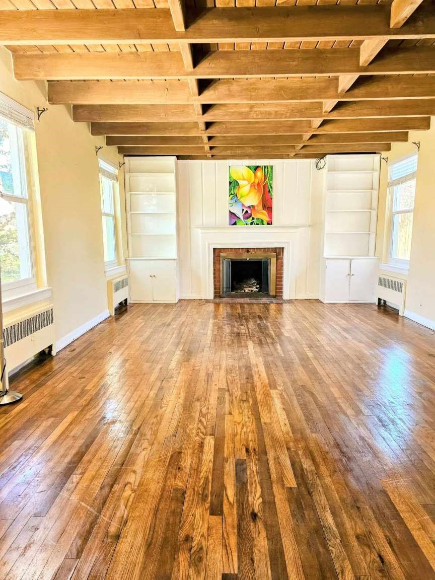 Living room with exposed wood beams, polished hardwood floors, and a fireplace between built-in shelves.