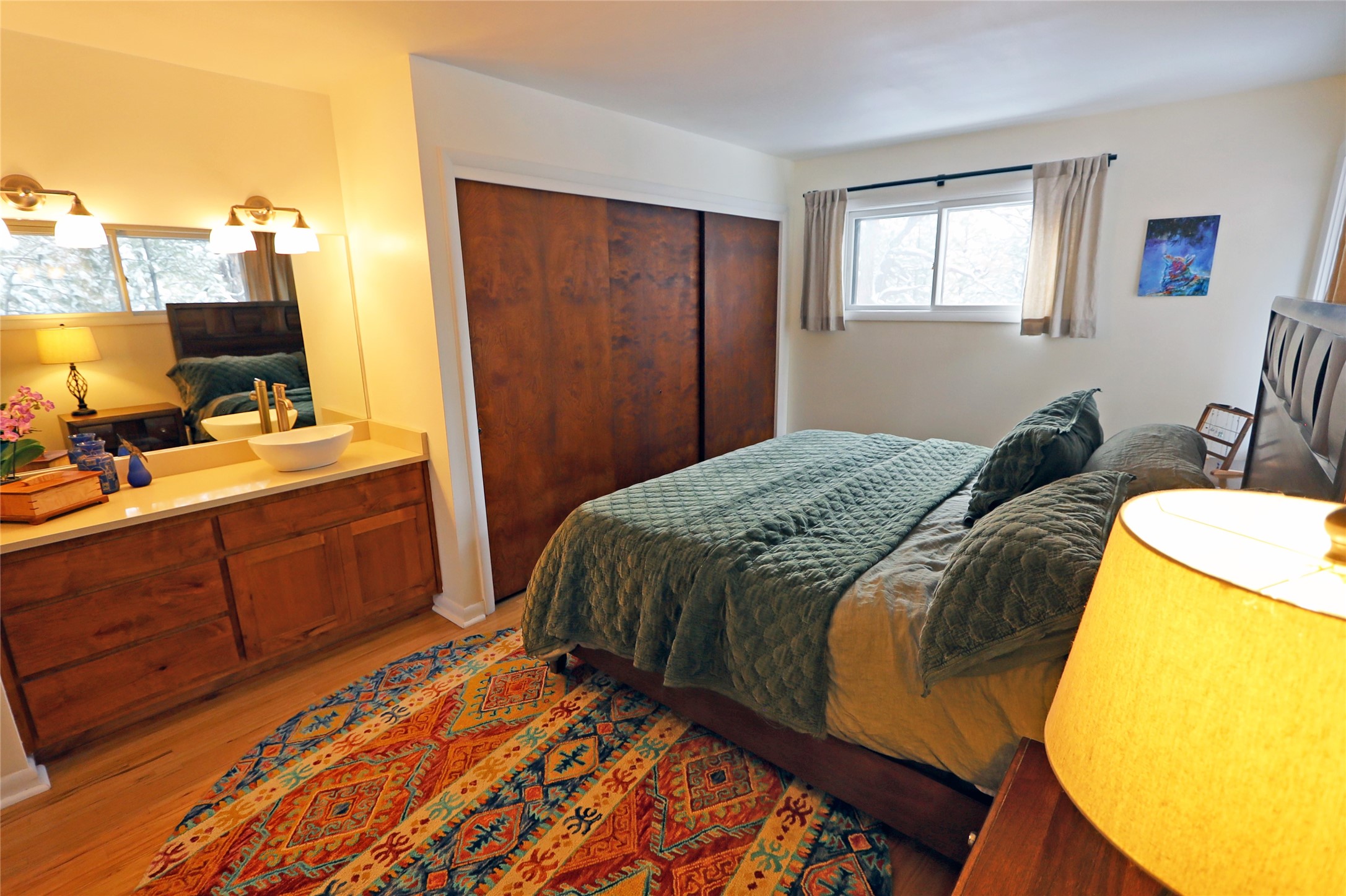 Bedroom with dark green bedding, wood closet doors, a vessel sink vanity, and a colorful patterned rug.