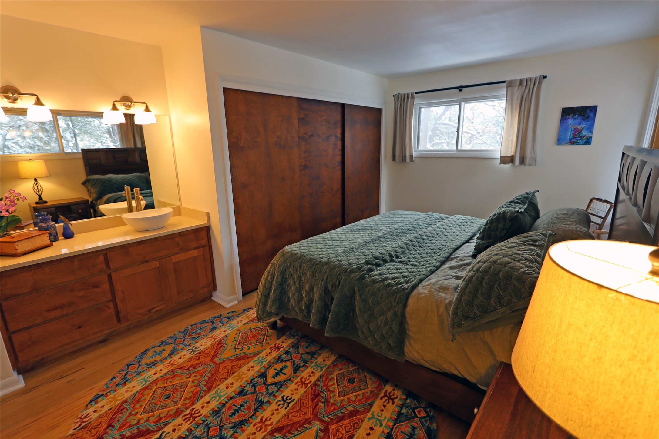 Bedroom with dark green bedding, wood closet doors, a vessel sink vanity, and a colorful patterned rug.