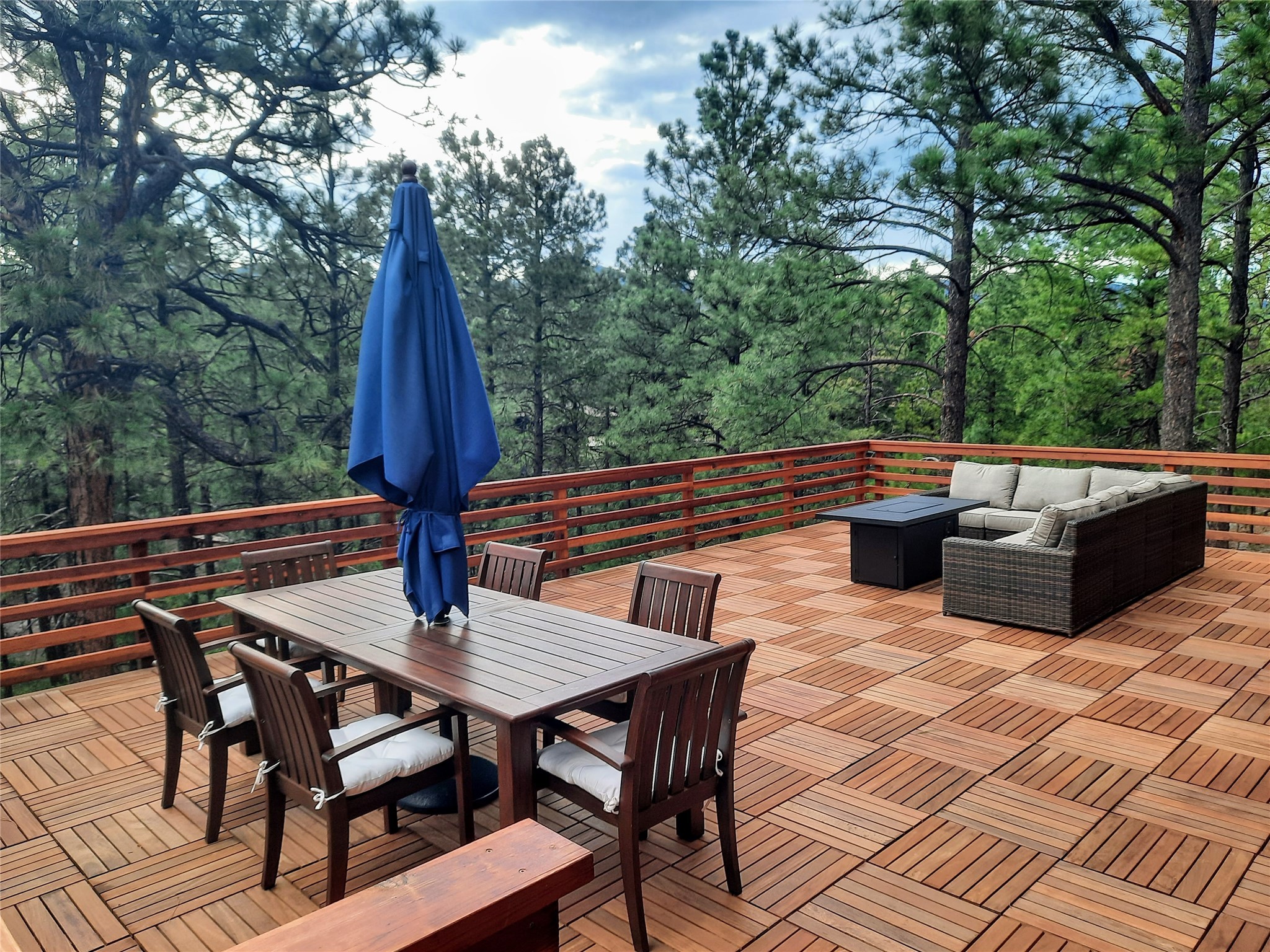 Wooden deck with dining and lounge seating overlooking pine trees.