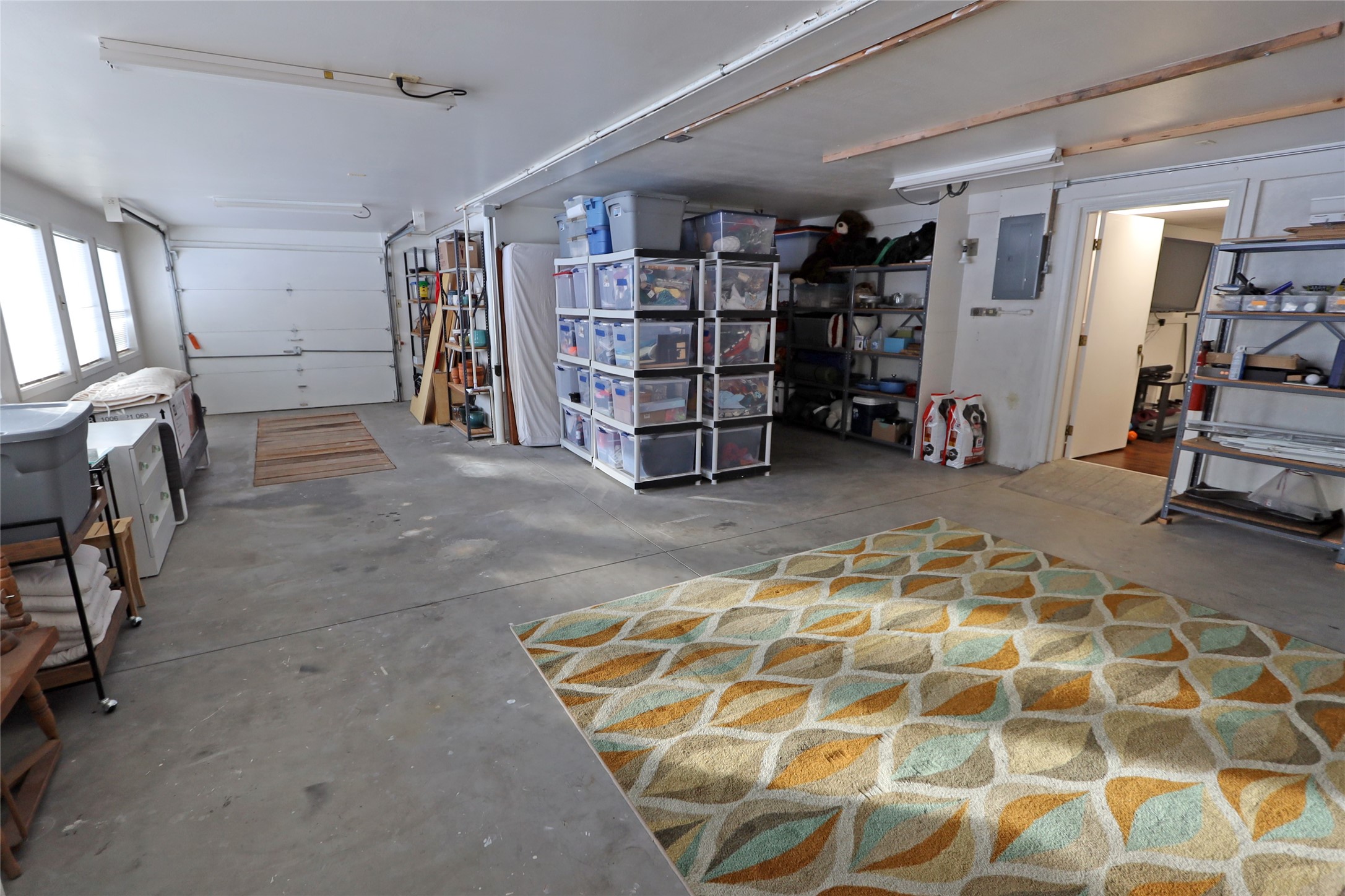 Garage with extensive storage shelving, plastic bins, and a large geometric-patterned rug.