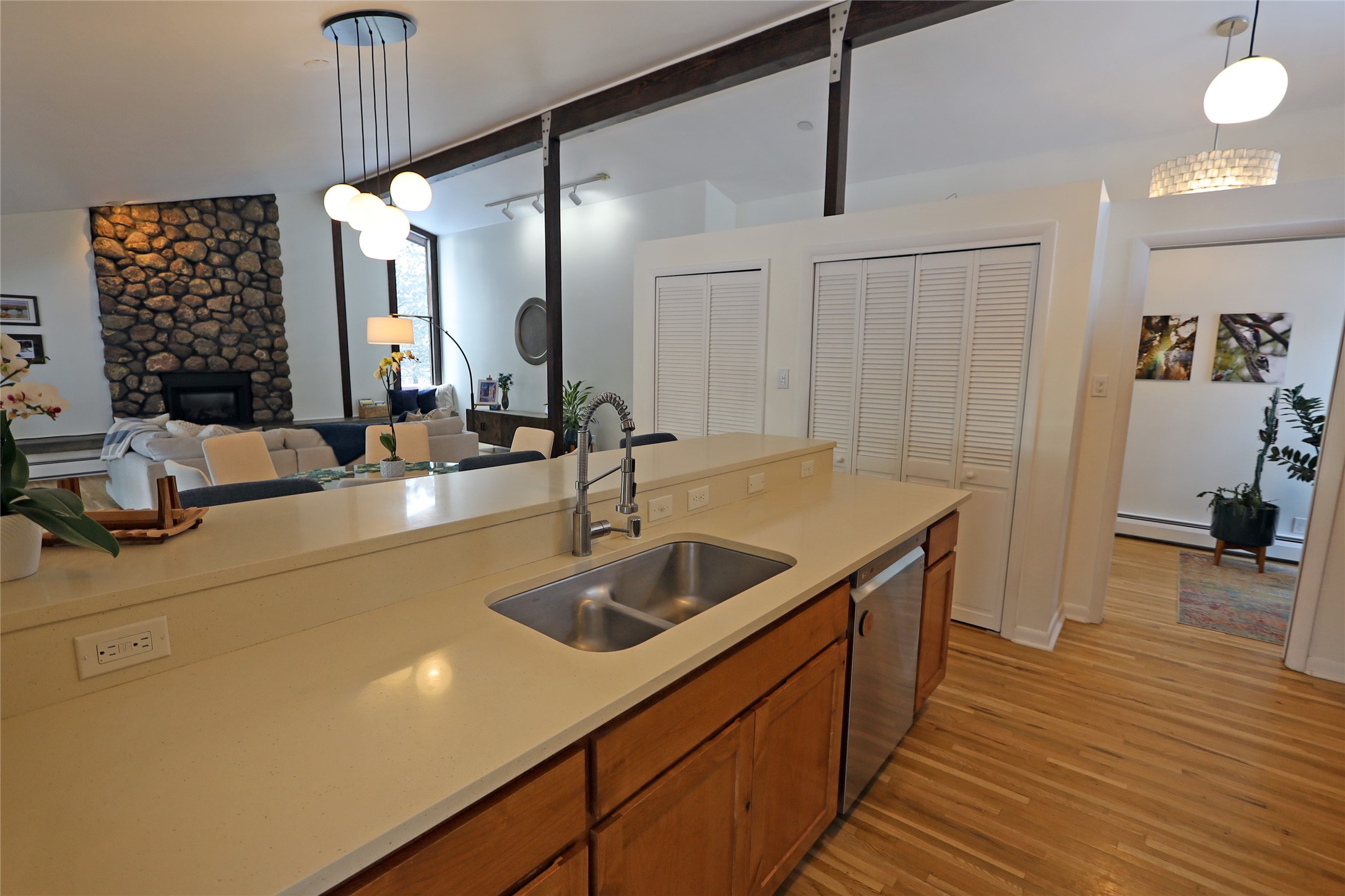 Open-plan kitchen with a long cream island, wood cabinets, and a stone fireplace in the living area.