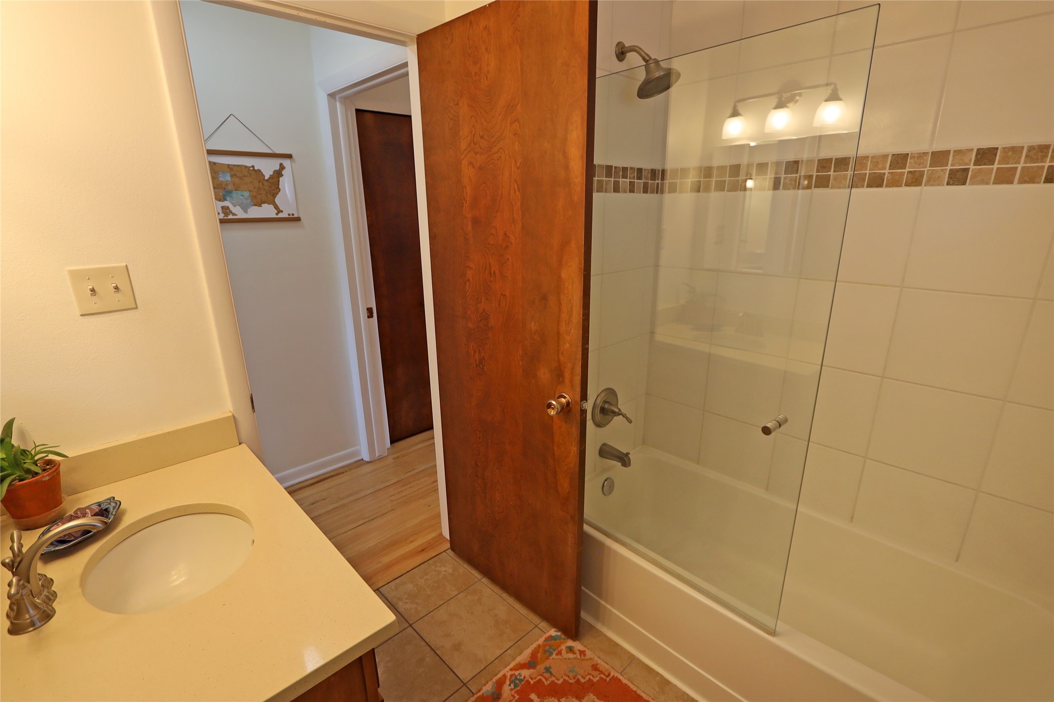 Bathroom with a glass-enclosed tub, tiled shower, and pale vanity beside an open wooden door.