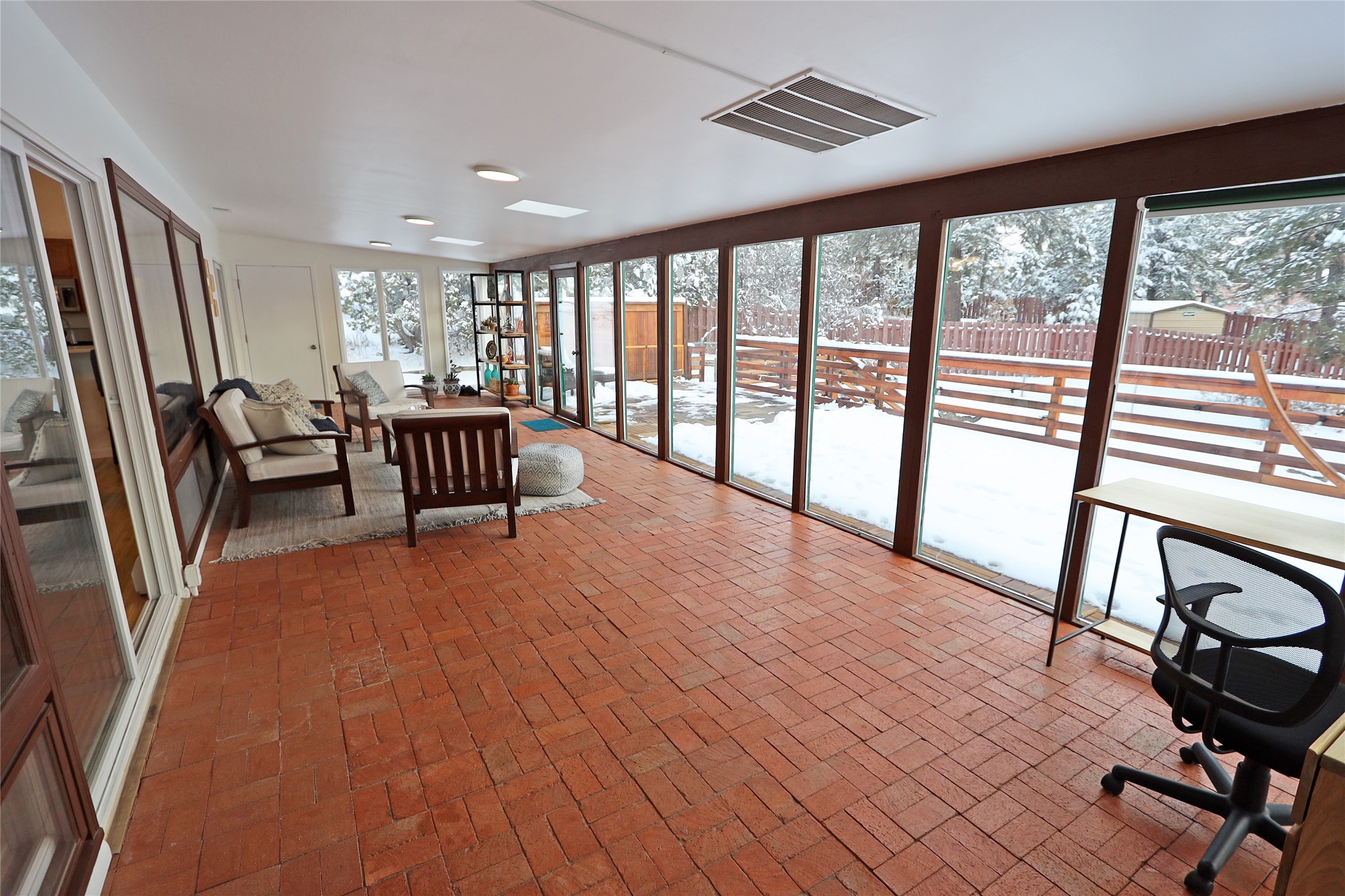 Sunroom with a red brick floor and tall windows overlooking a snowy deck.