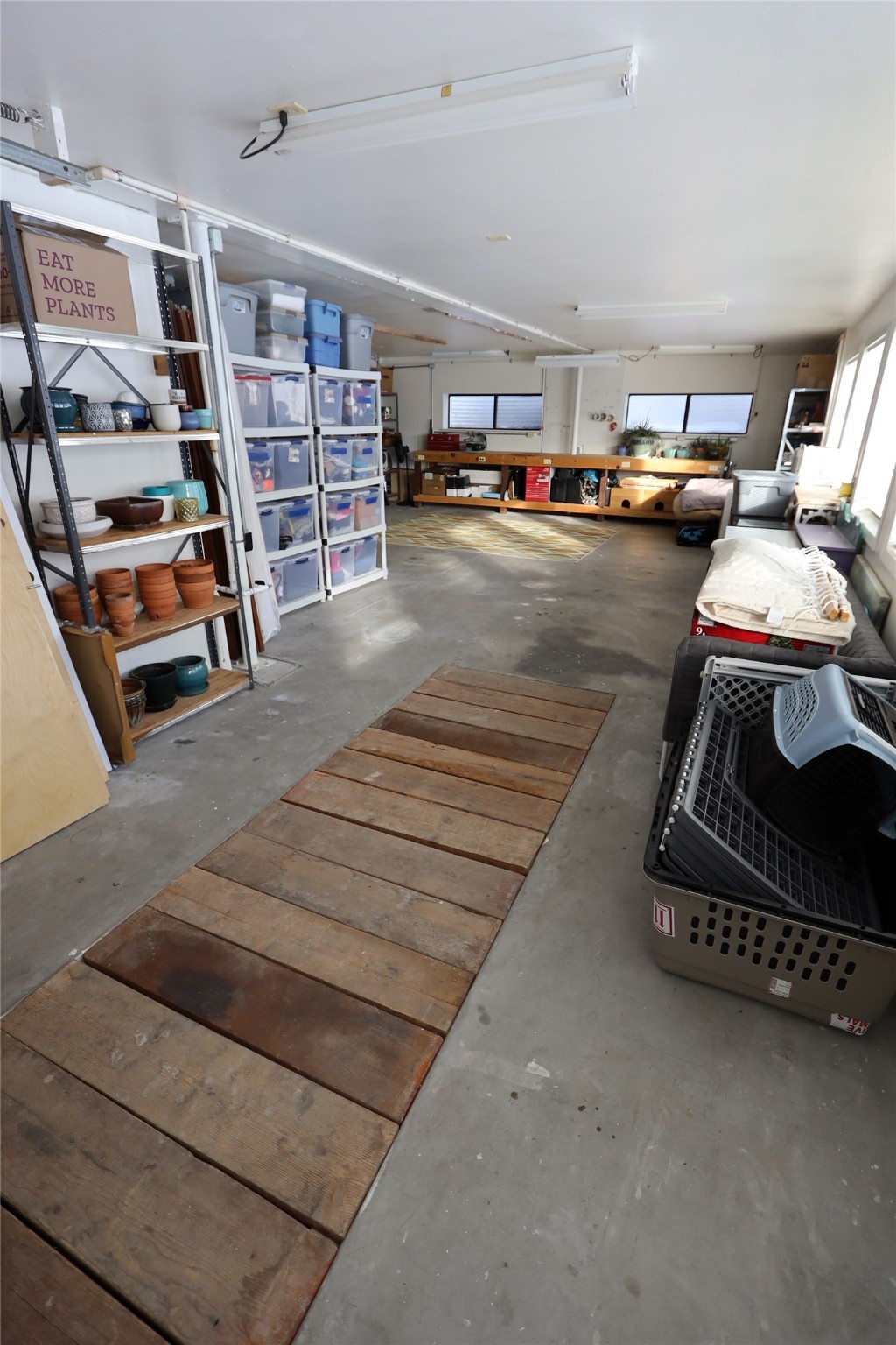 Garage with storage shelves, a long workbench, and wooden planks laid across the concrete floor.