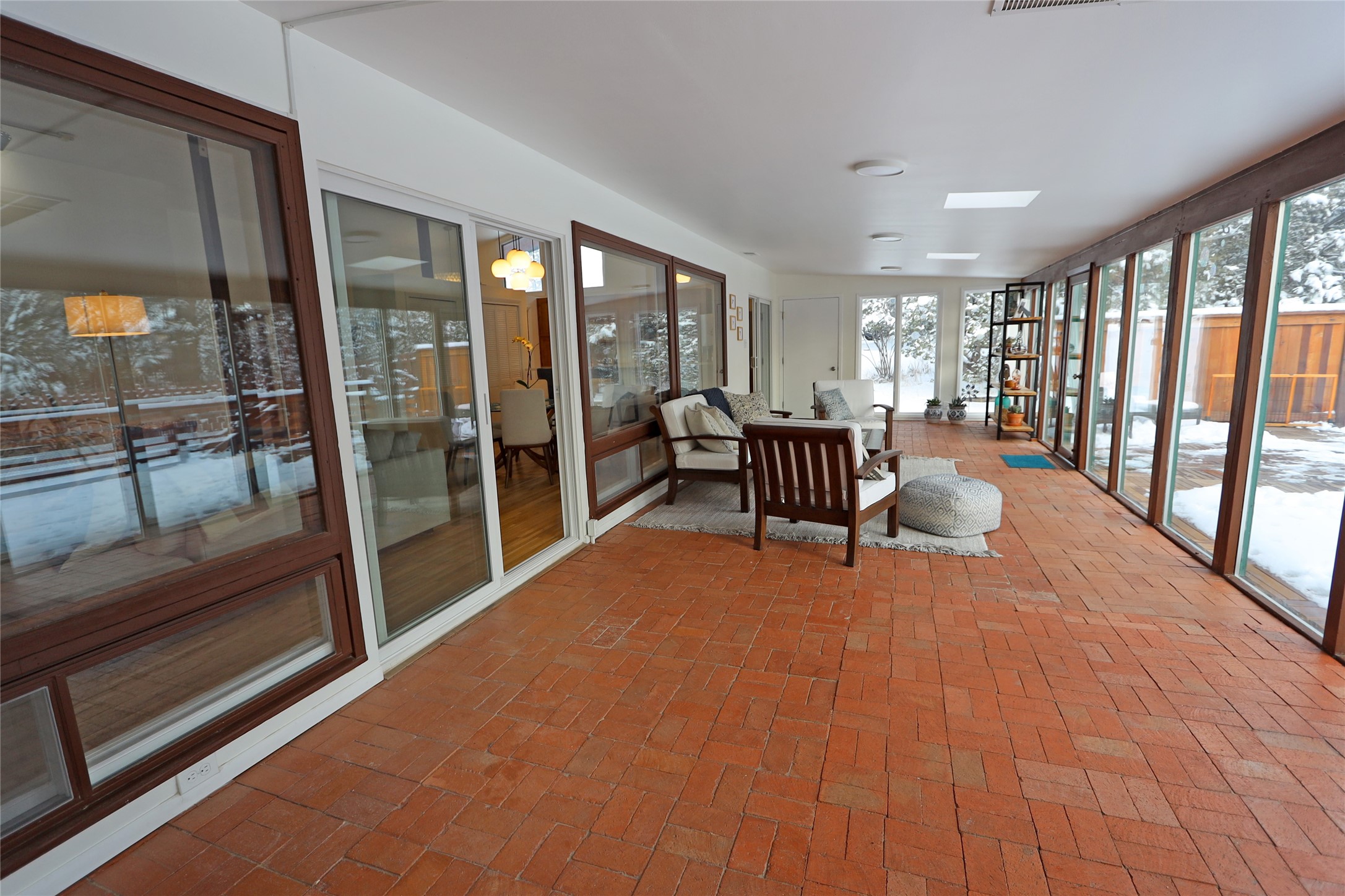 Sunroom with a red brick floor, expansive windows, and seating overlooking a snowy yard.