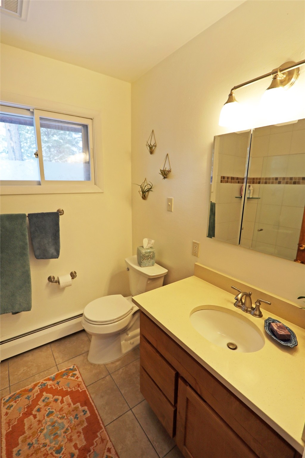 Bathroom with a wood vanity, mirrored medicine cabinet, tiled shower, and orange patterned rug.