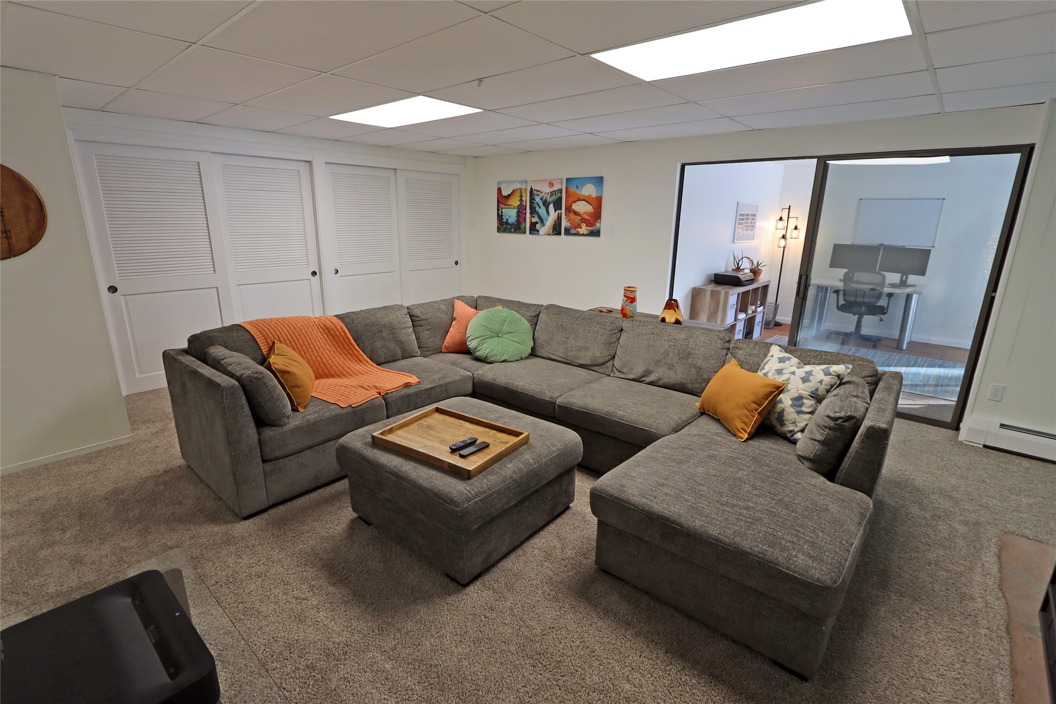 Furnished living room with a gray sectional, ottoman, and glass doors to an adjoining office.