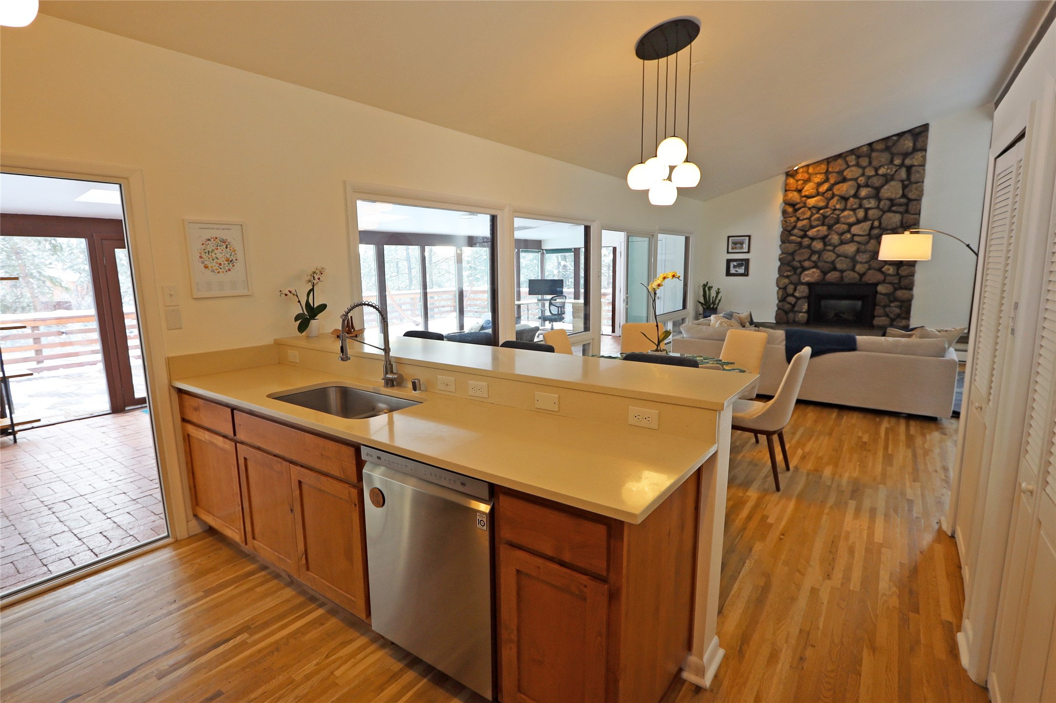 Open-plan kitchen with a wood island and stainless-steel dishwasher, overlooking a living room with a stone fireplace.
