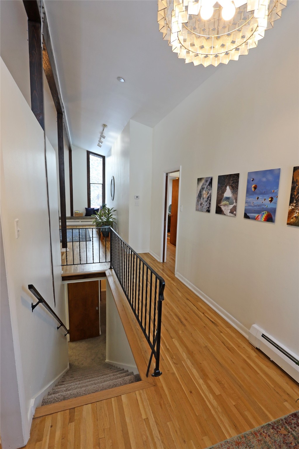 Upper-level hallway and stair landing with hardwood floors, black railing, and a geometric chandelier.