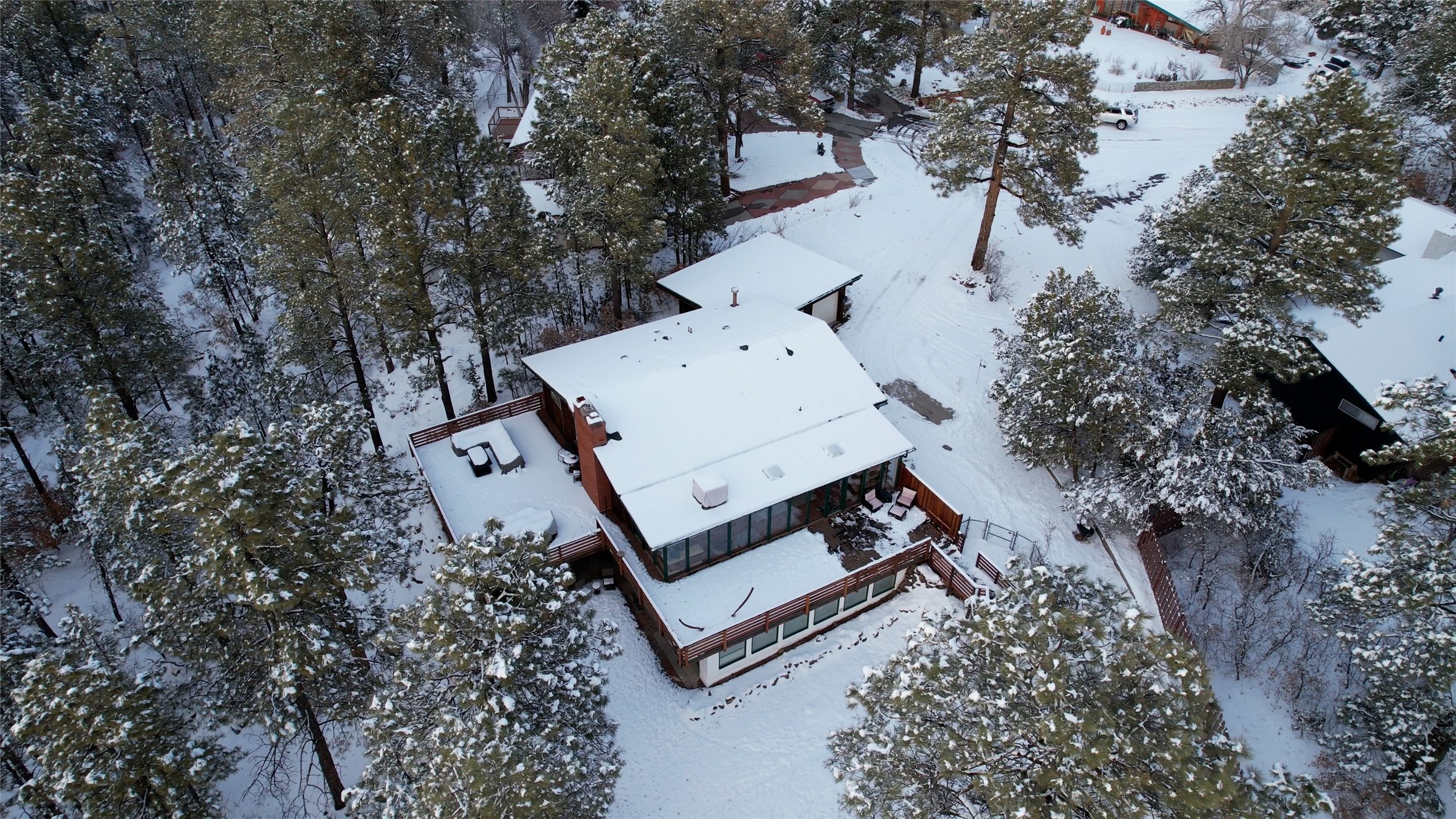 Aerial view of a multi-level home and decks blanketed in snow among pine trees.