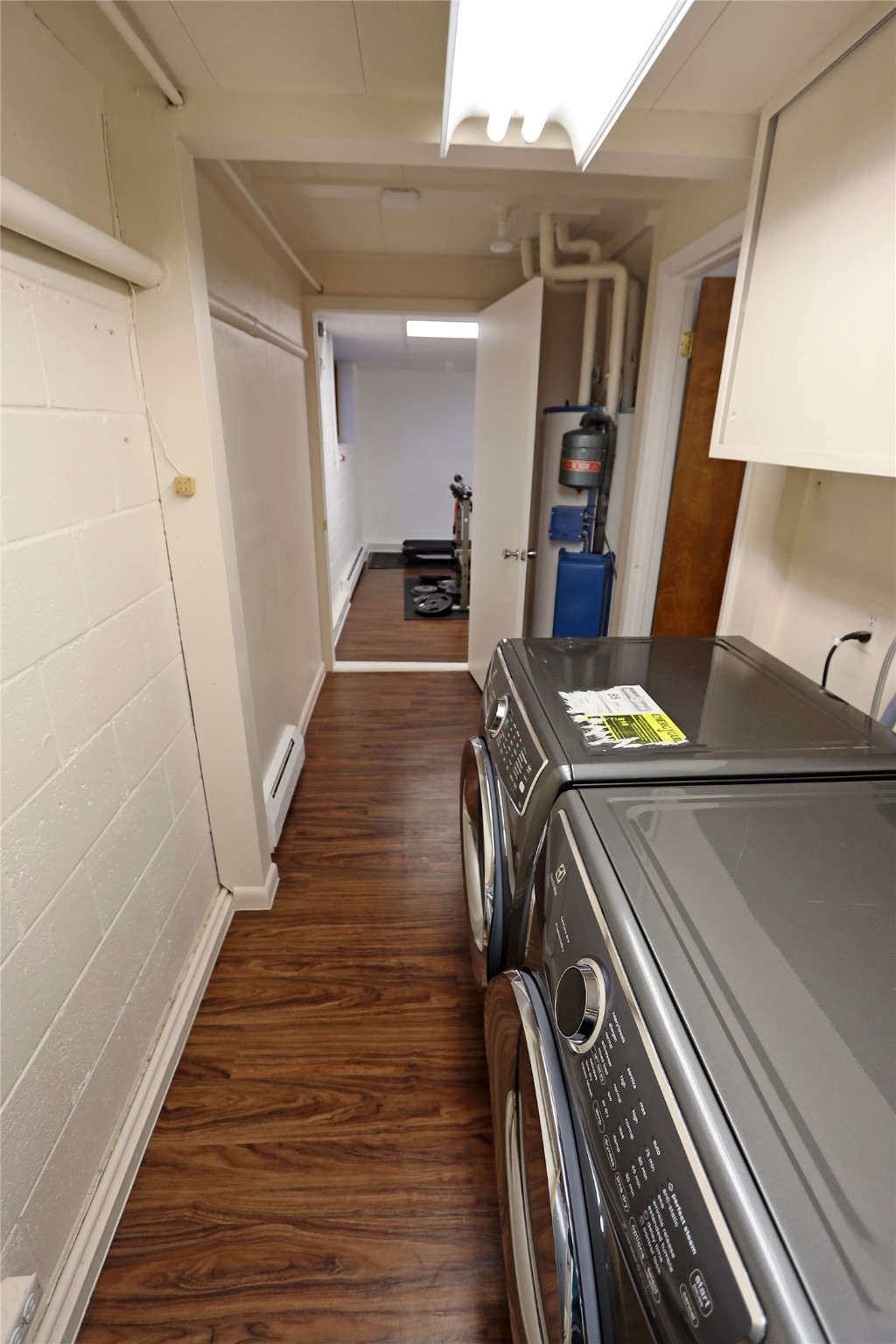 Laundry room with washer and dryer, wood-look flooring, and an open doorway to an exercise room.