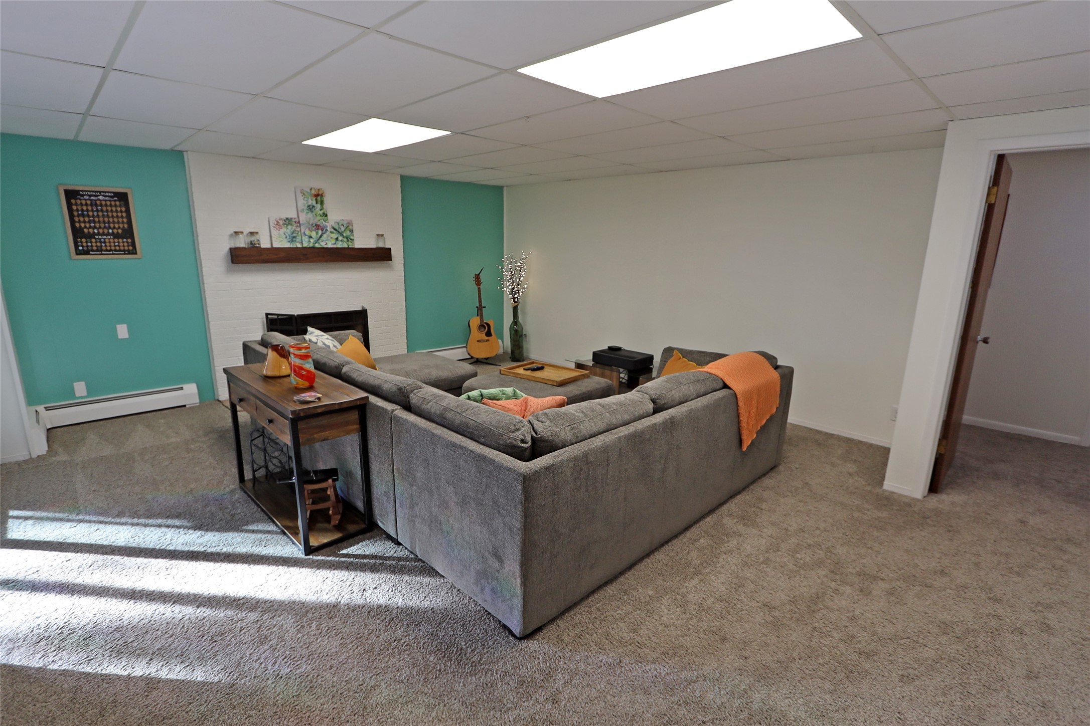 Living room with a gray sectional, turquoise accent walls, white brick fireplace wall, and sunlit carpet.