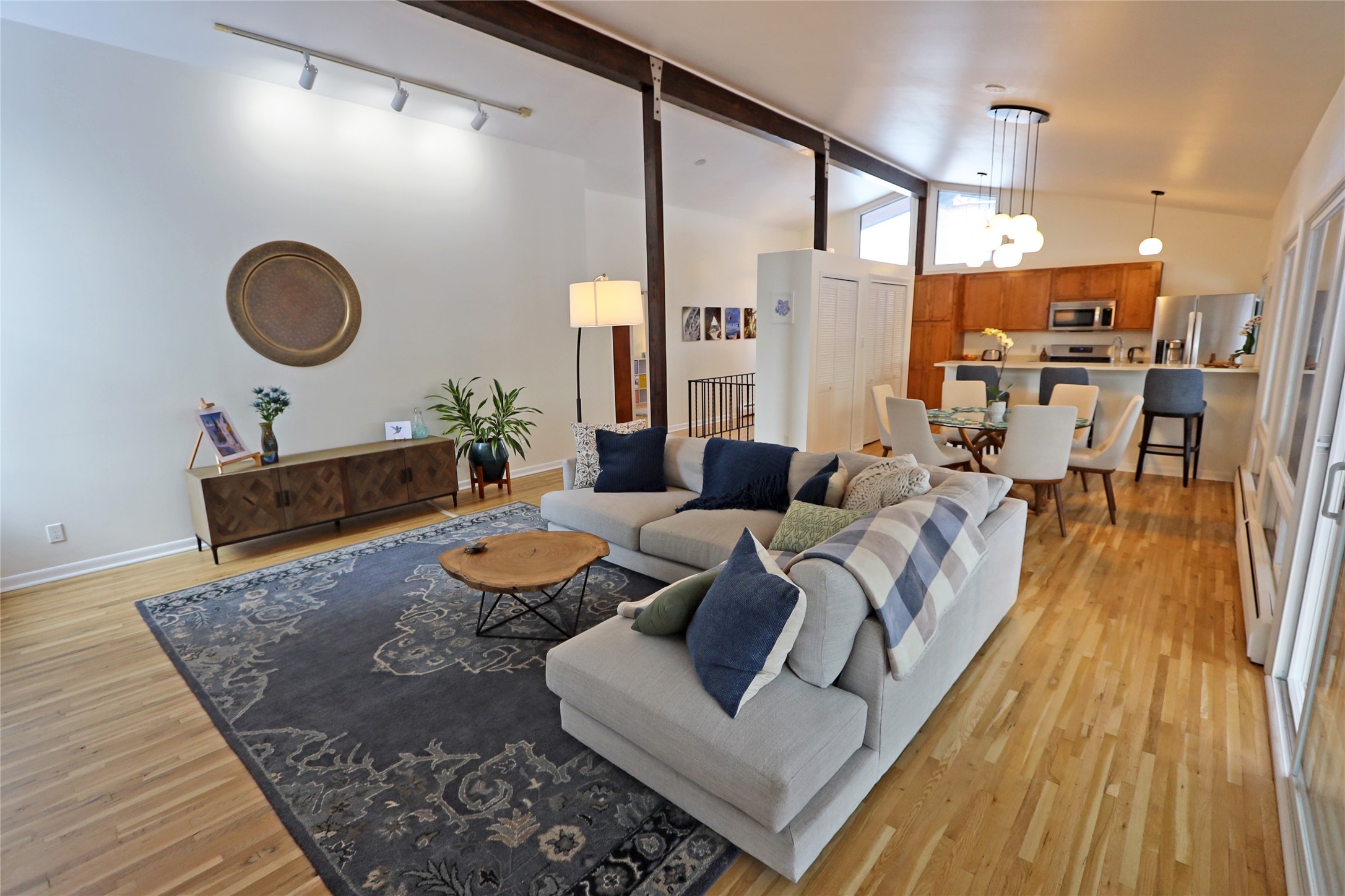 Open-plan living room with a gray sectional, patterned rug, exposed beams, and dining area beyond.