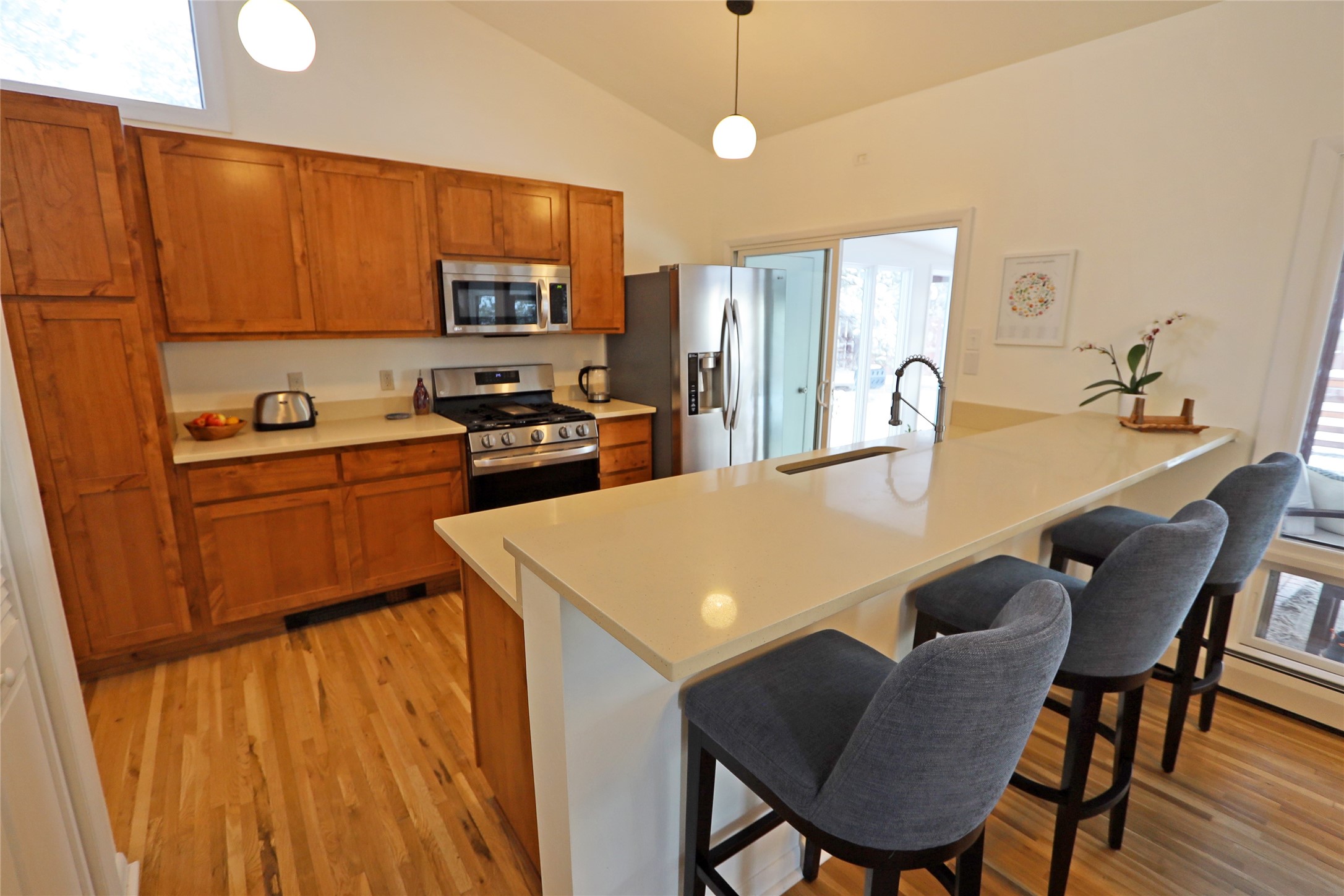 Kitchen with warm wood cabinets, stainless steel appliances, and a large island with gray bar stools.