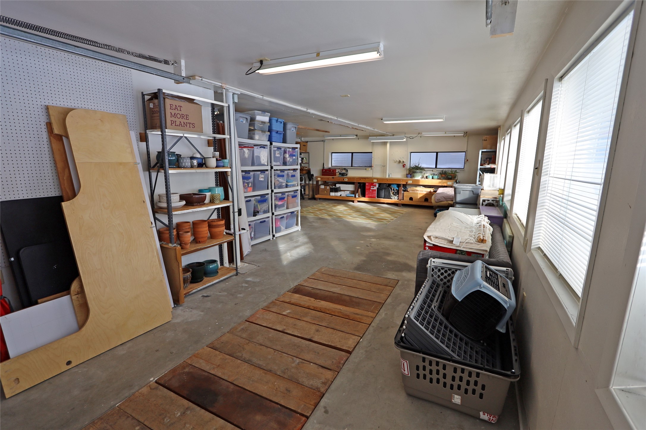 Garage workshop with storage shelves, a rear workbench, and windows along one wall.