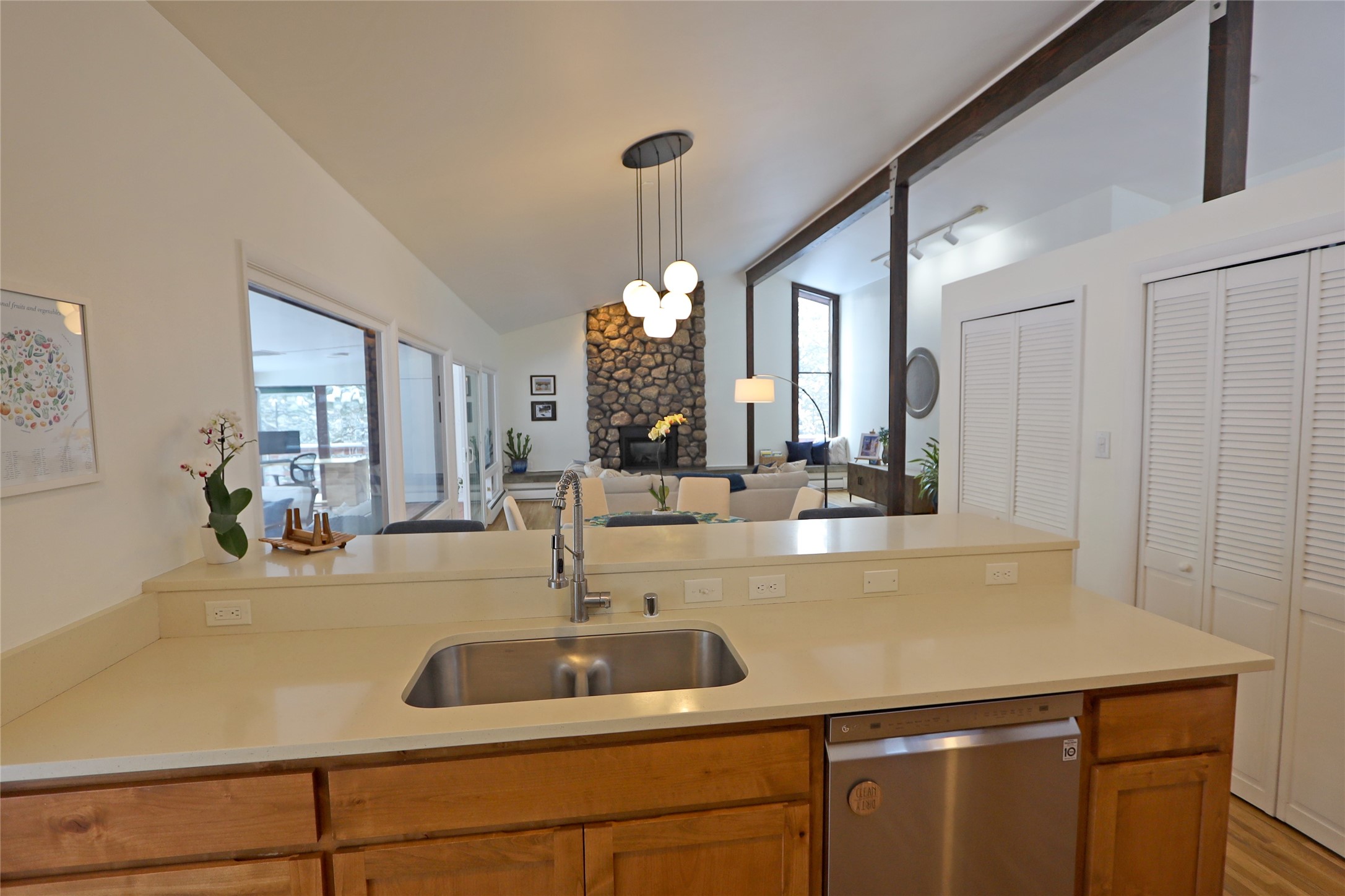 Open-plan kitchen with wood cabinets and a wide counter overlooking a living room with a stone fireplace.