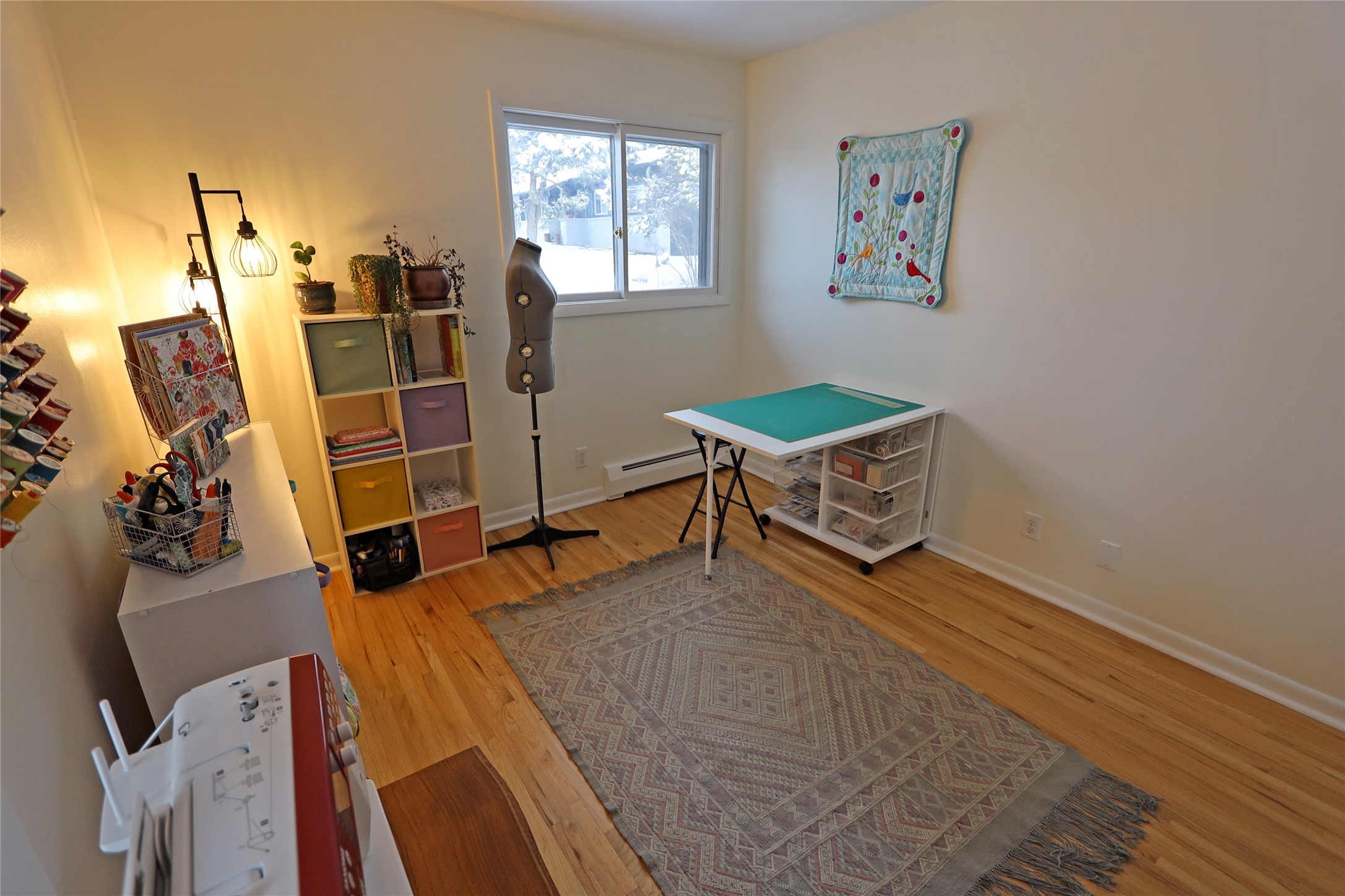 Craft room with a turquoise cutting mat, sewing supplies, and a dress form beside a snowy window.