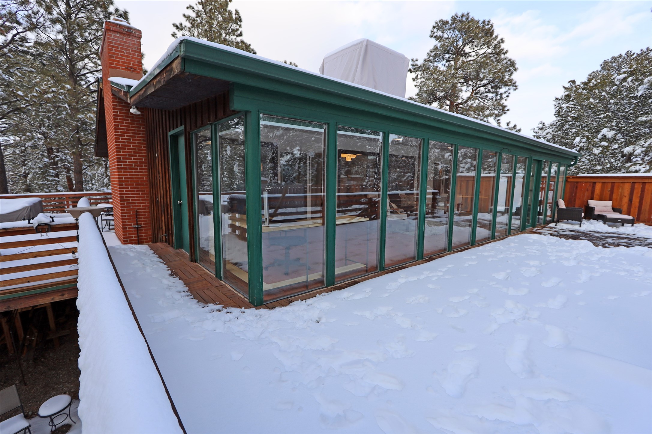 Home exterior with a glass-enclosed sunroom and deck covered in snow.