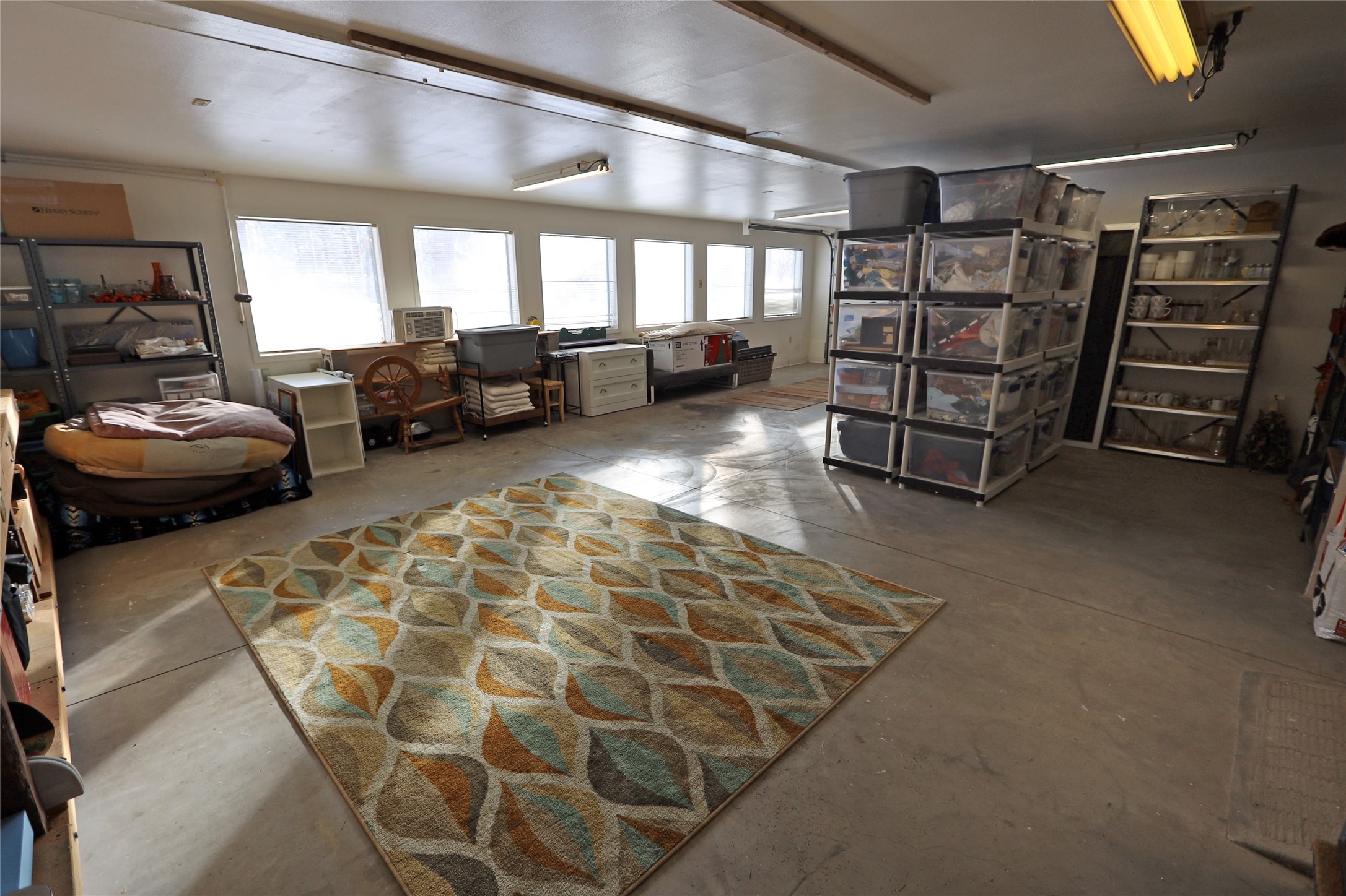Spacious garage with concrete floors, bright windows, extensive storage shelving, and a large patterned rug.