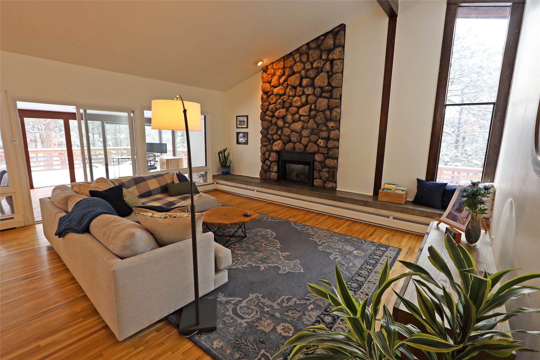 Living room with a floor-to-ceiling stone fireplace, hardwood floors, and windows overlooking a snowy deck.
