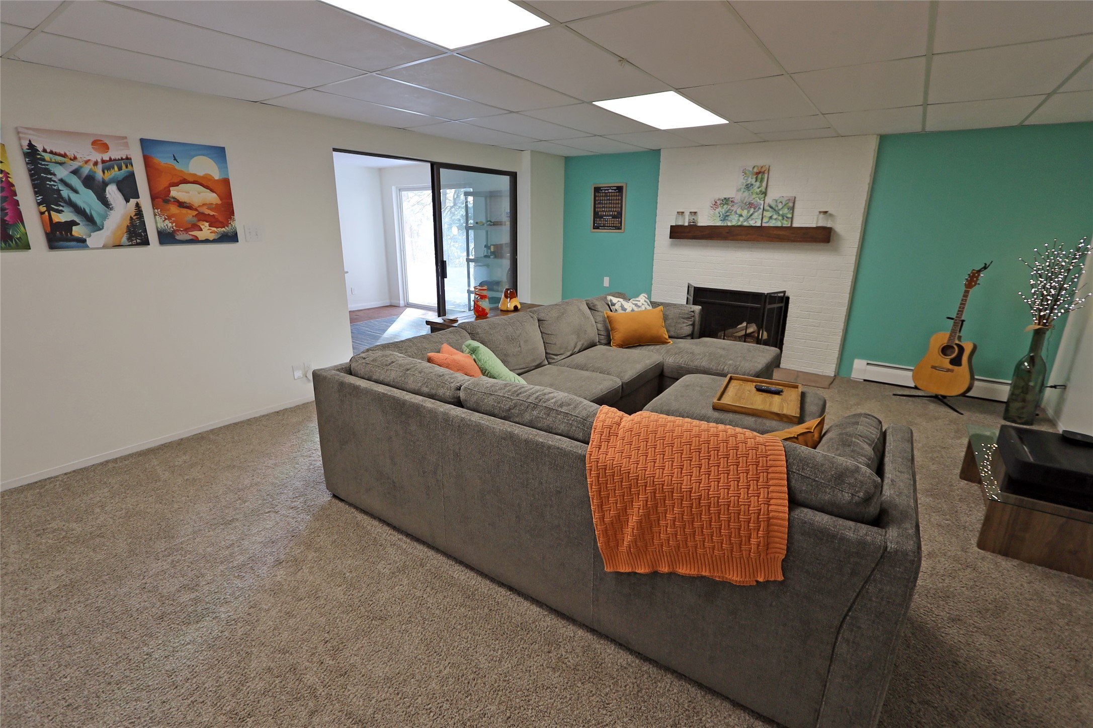 Living room with a gray sectional, orange throw, turquoise walls, and white brick fireplace.