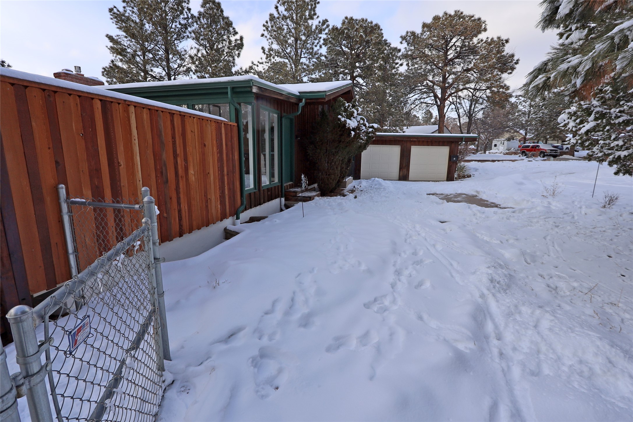 Wood-sided home and detached two-car garage beside a snow-covered driveway.