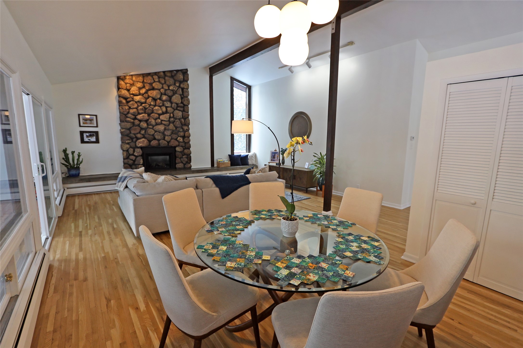 Open-plan living and dining room with a stone fireplace, hardwood floors, and a round glass dining table.