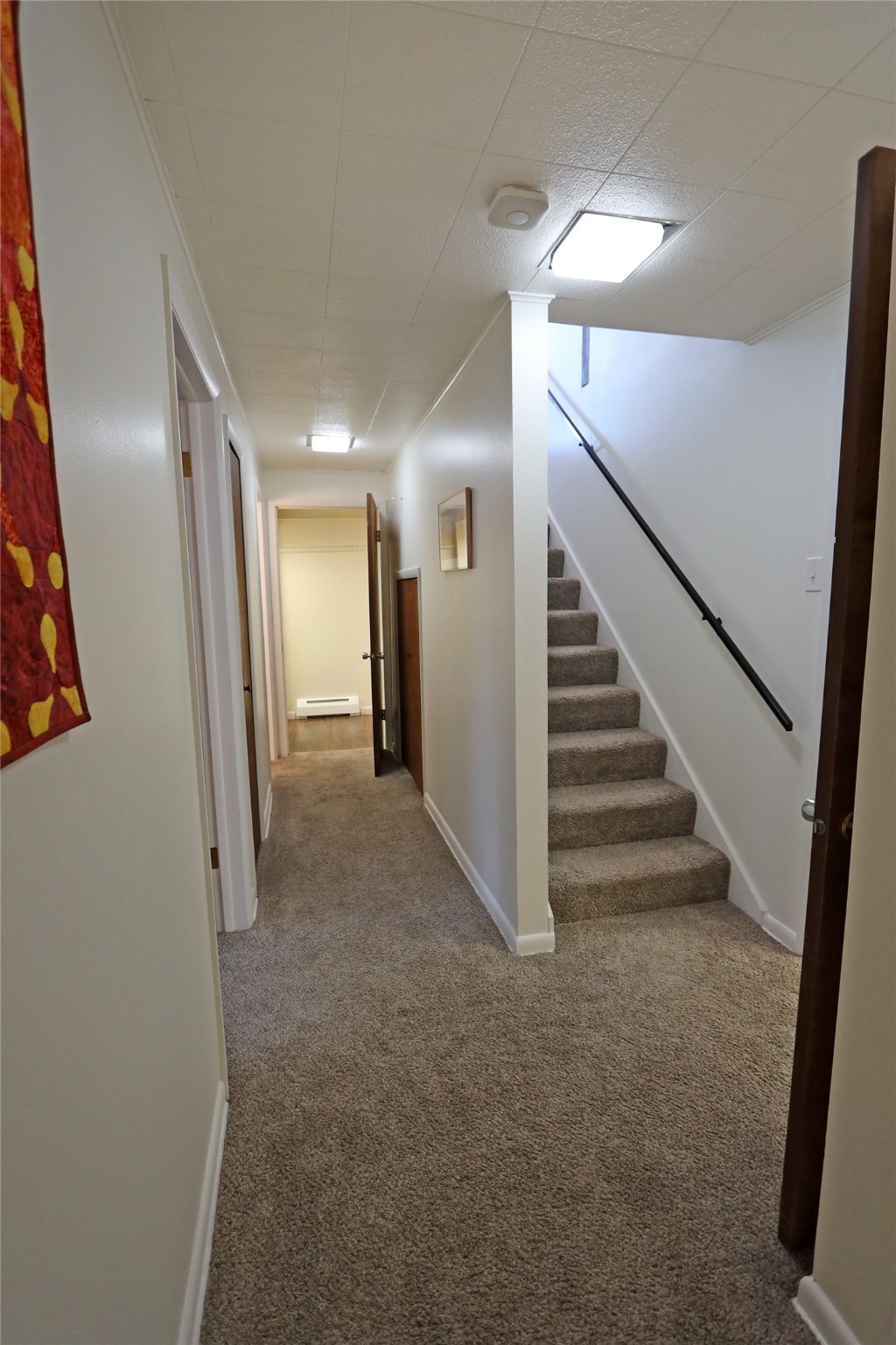 Carpeted hallway leading to a staircase with a dark handrail and several doorways.