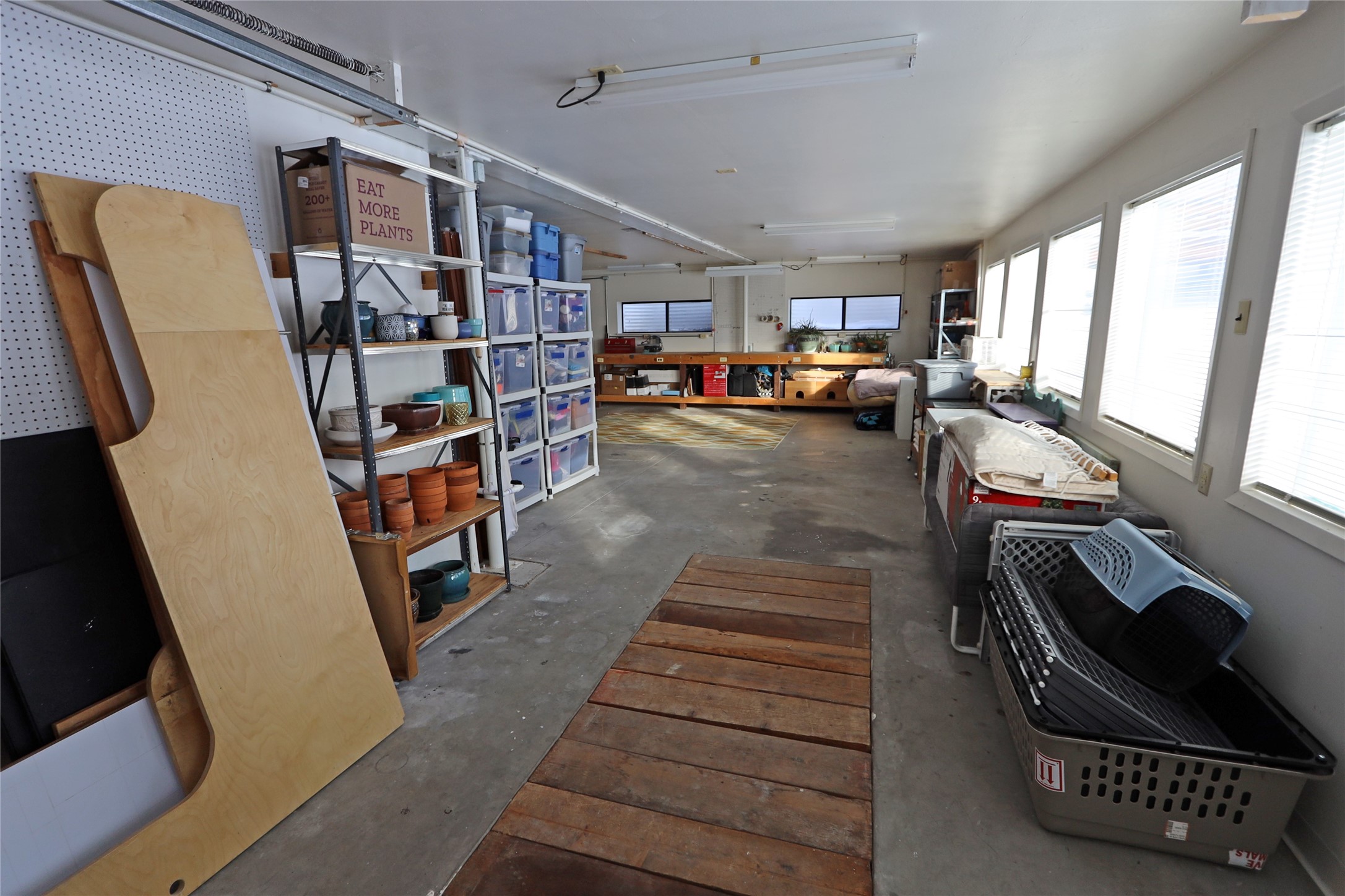 Garage workshop with a long wooden workbench, storage shelves, and windows along one wall.