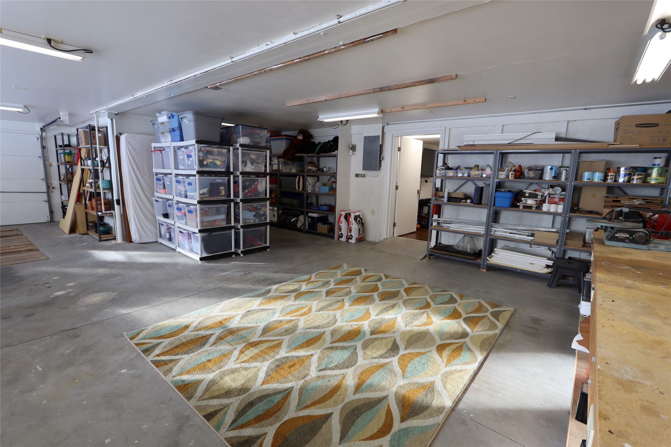 Garage with extensive shelving, storage bins, a workbench, and a patterned rug.