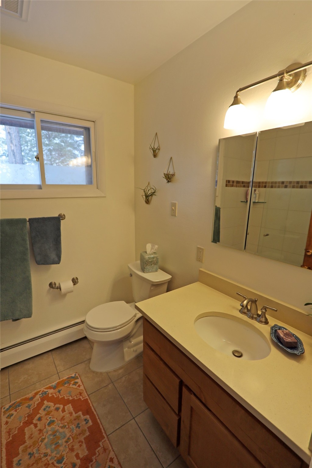 Bathroom with a wood vanity, mirrored cabinet, toilet, and window with frosted glass.