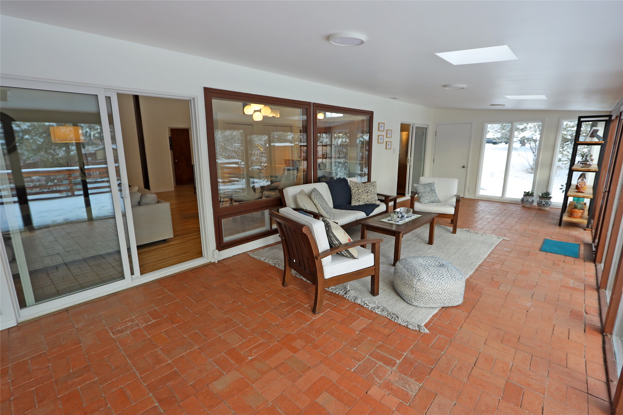 Furnished sunroom with terracotta brick floors, wood-framed seating, and large windows overlooking snow.