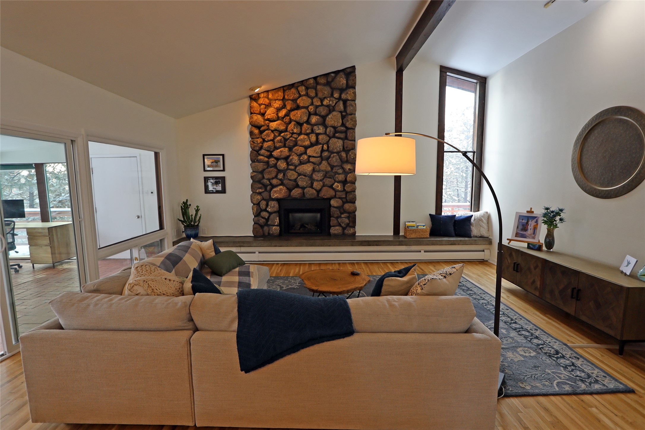 Living room with a tall stone fireplace, vaulted ceiling, and beige sectional sofa.