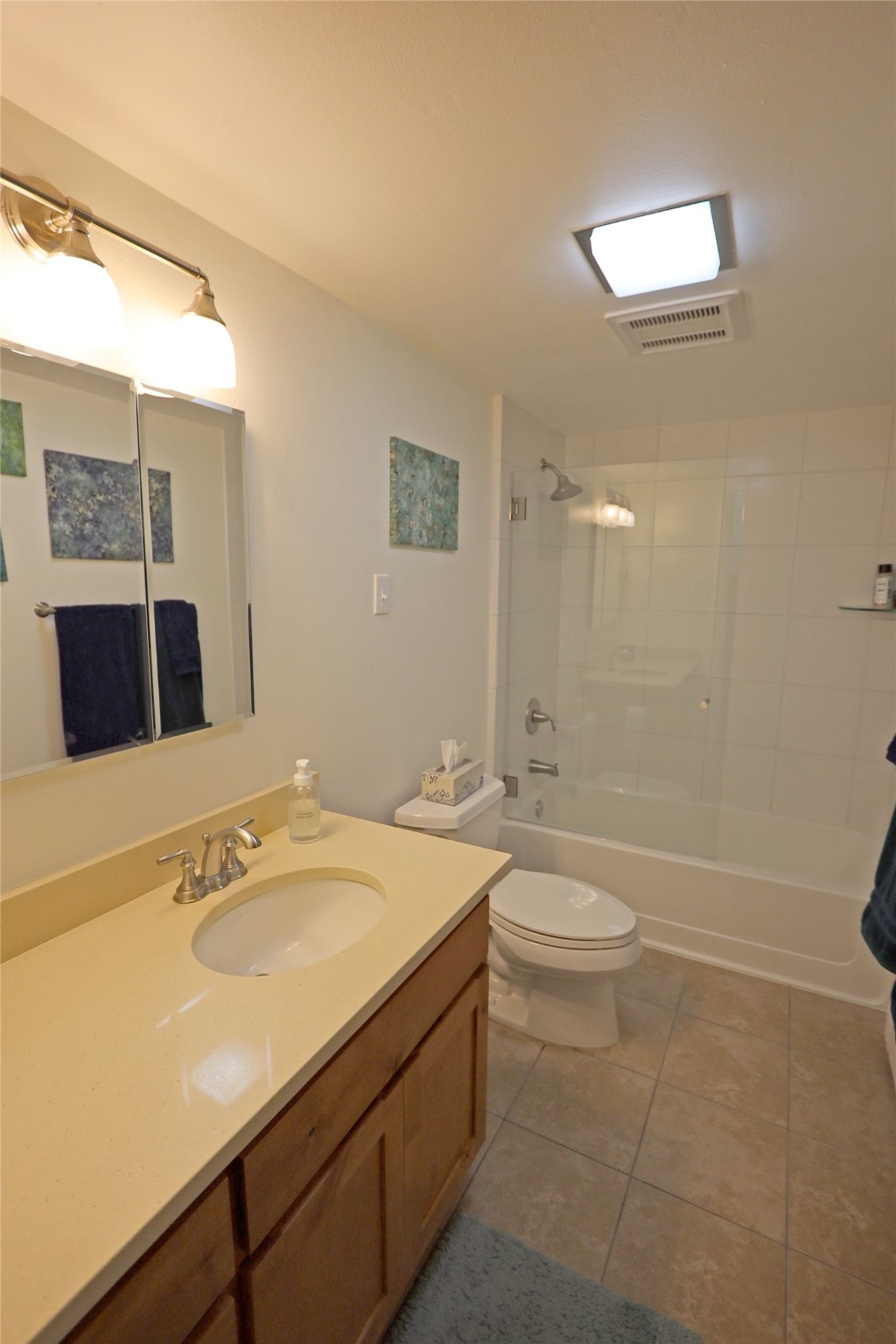 Bathroom with a wood vanity, mirrored cabinet, and white-tiled tub and shower.