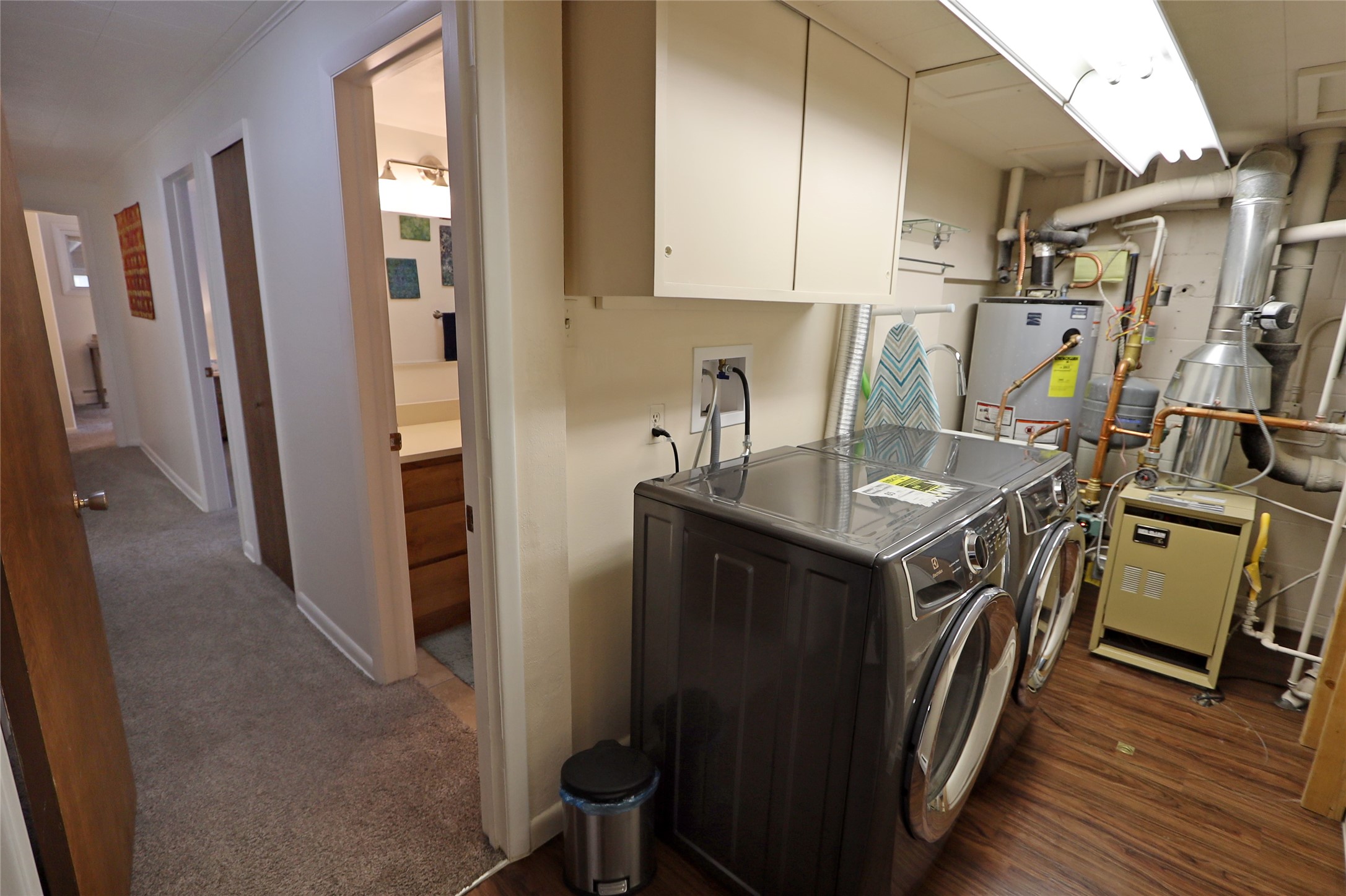 Laundry room with front-loading washer and dryer, wall cabinets, and exposed utility equipment.