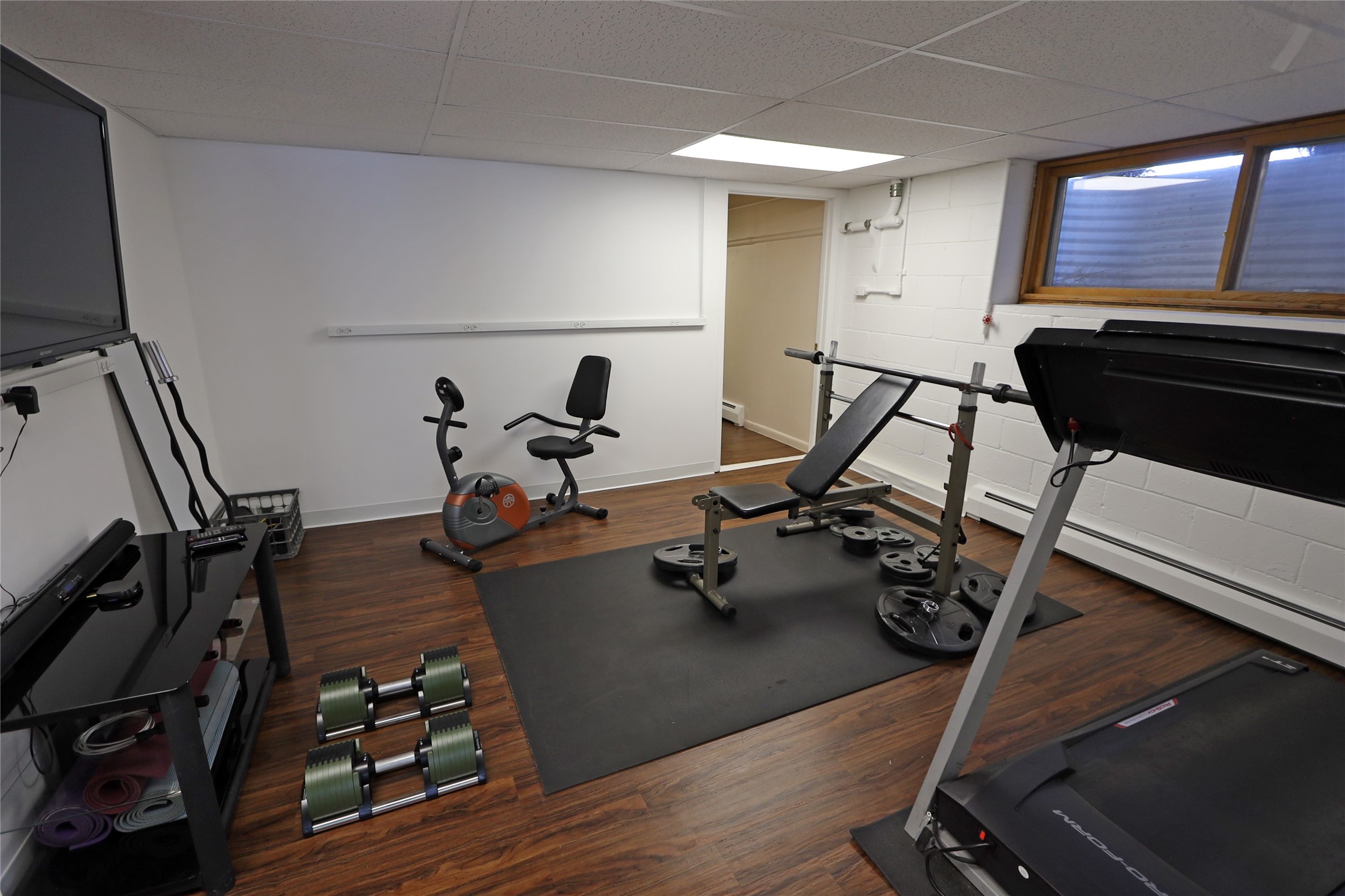 Home gym with treadmill, weight bench, exercise bike, and weights on a black workout mat.