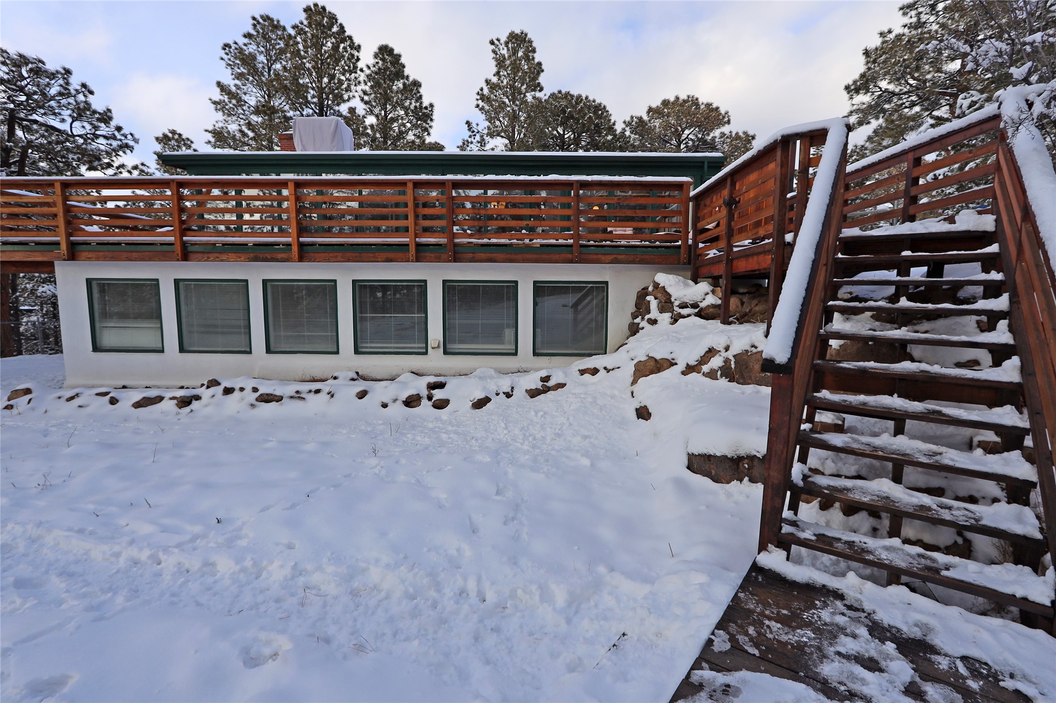 Snow-covered home exterior with a long wooden deck and a large staircase.