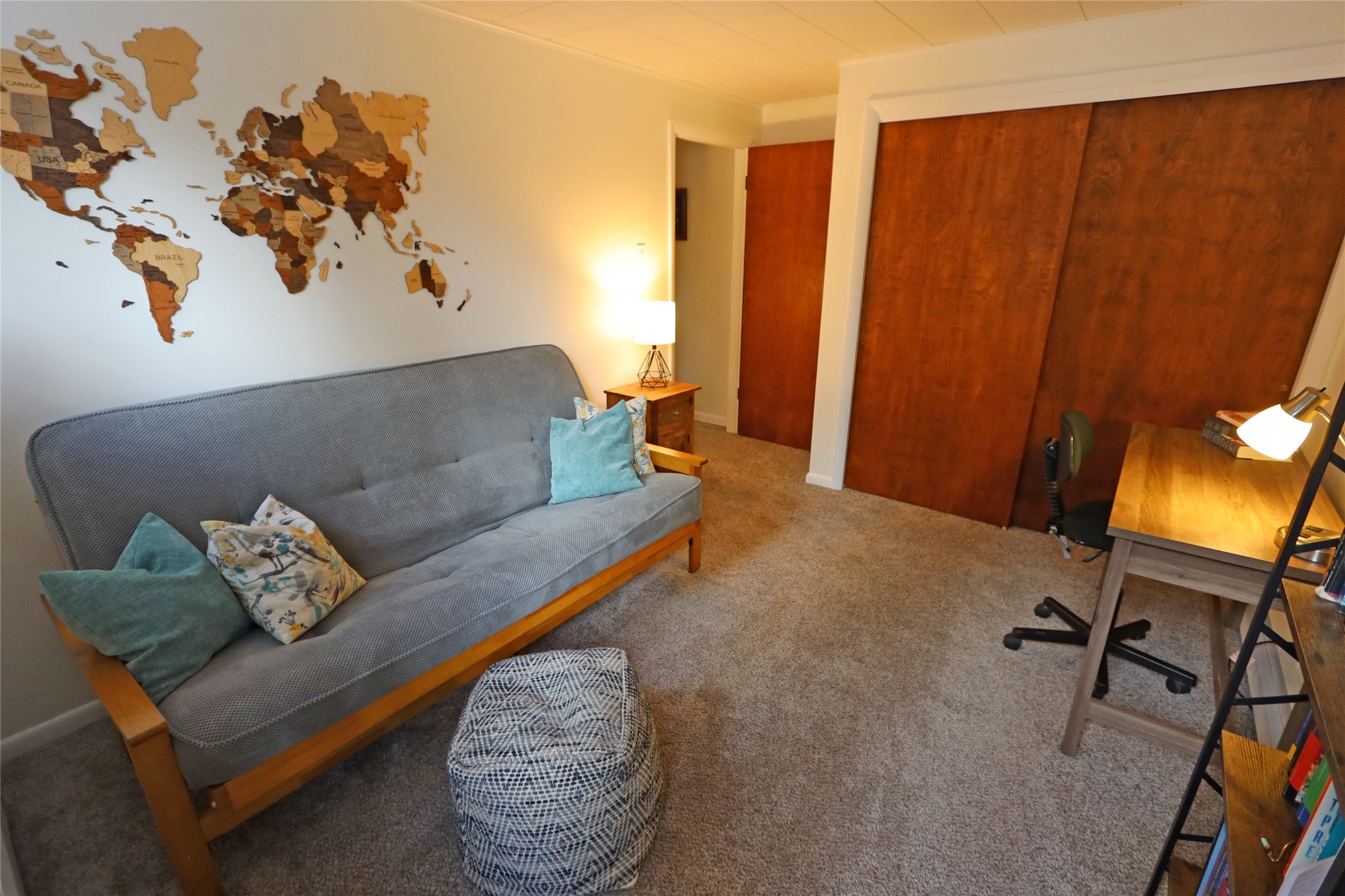 Furnished office with a gray futon, wooden desk, and large wooden sliding closet doors.