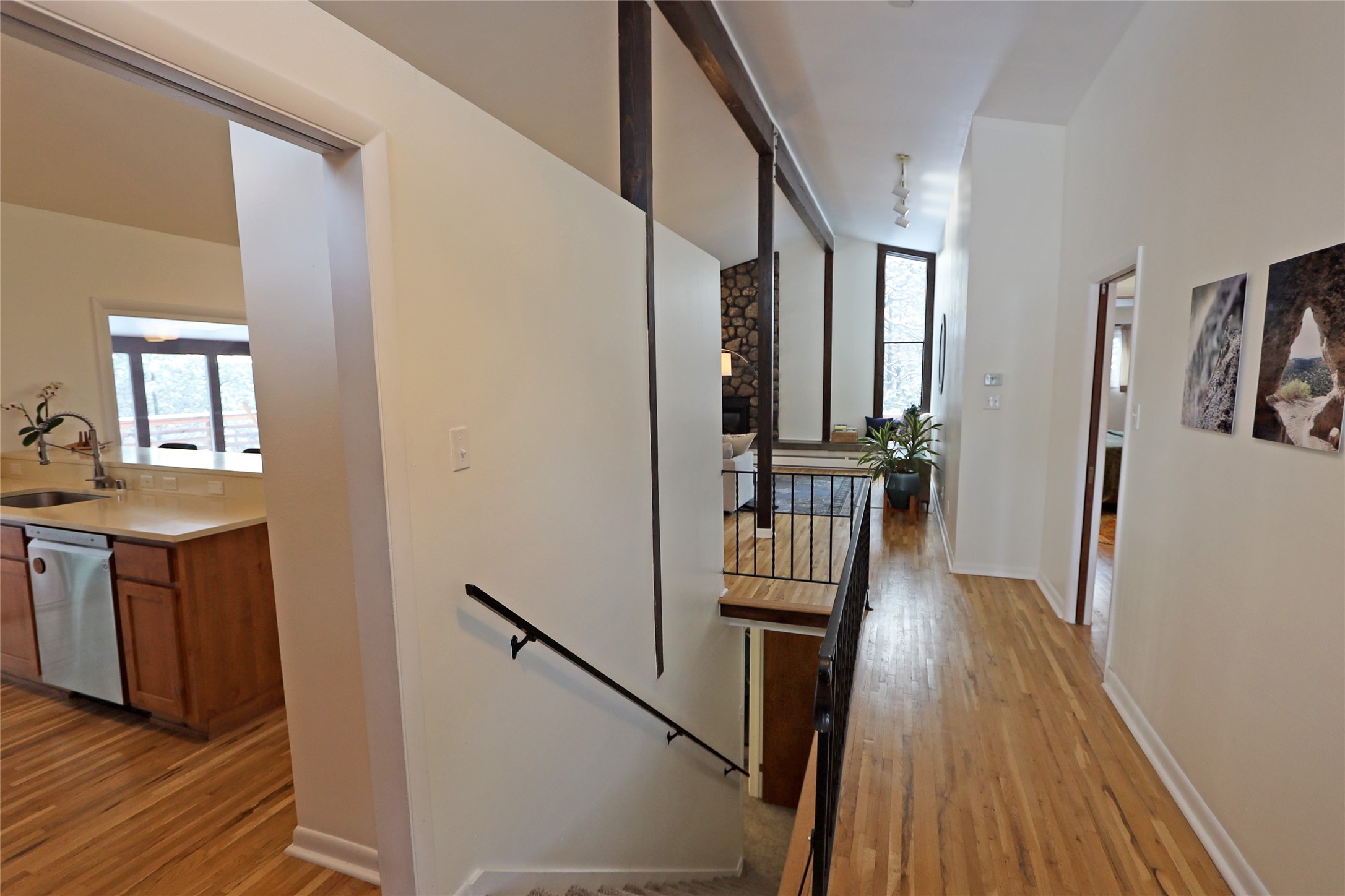 Hardwood hallway overlooks a stairwell and living area with dark beams and black metal railings.