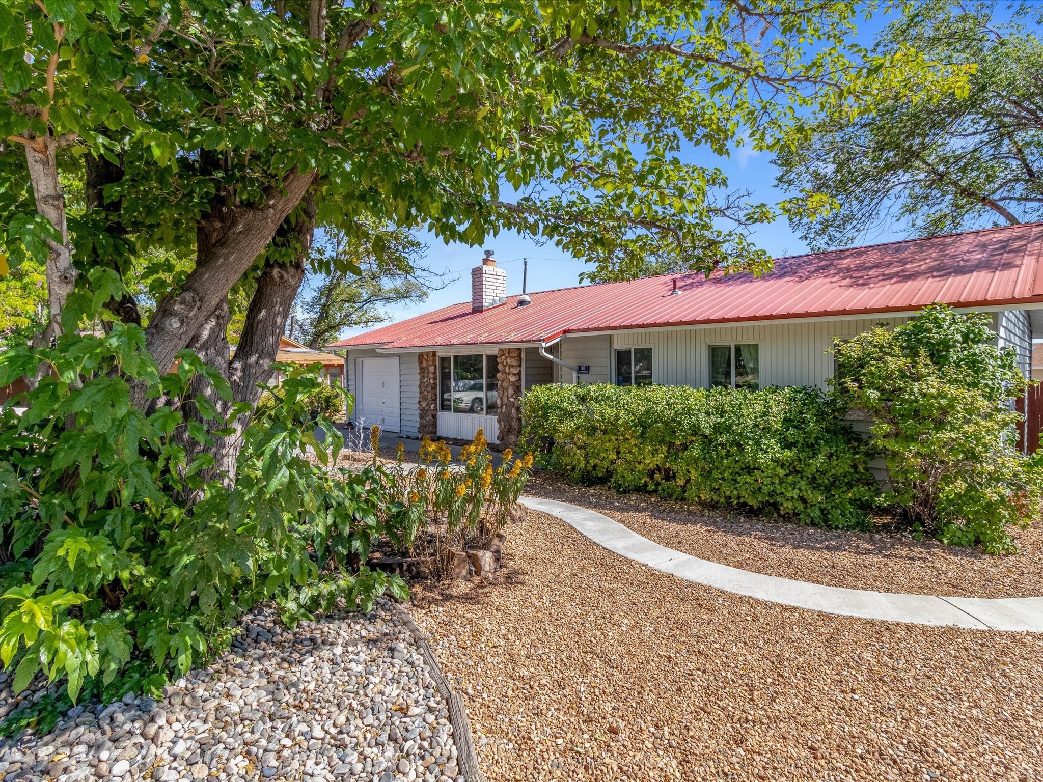 Single-story home with a red metal roof, stone window accents, and a curved walkway through gravel landscaping.